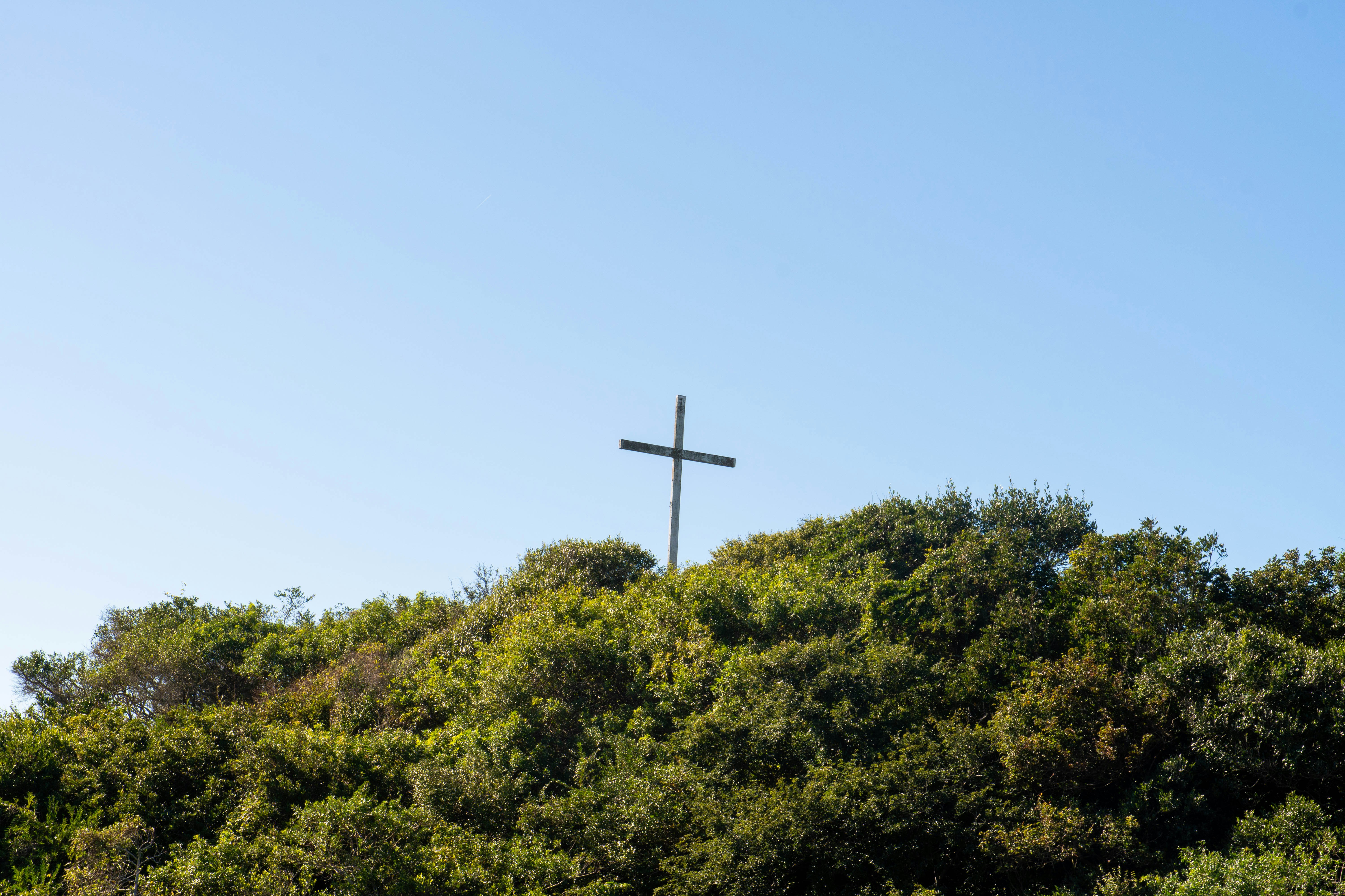 A cross stands atop a lush, green hill.