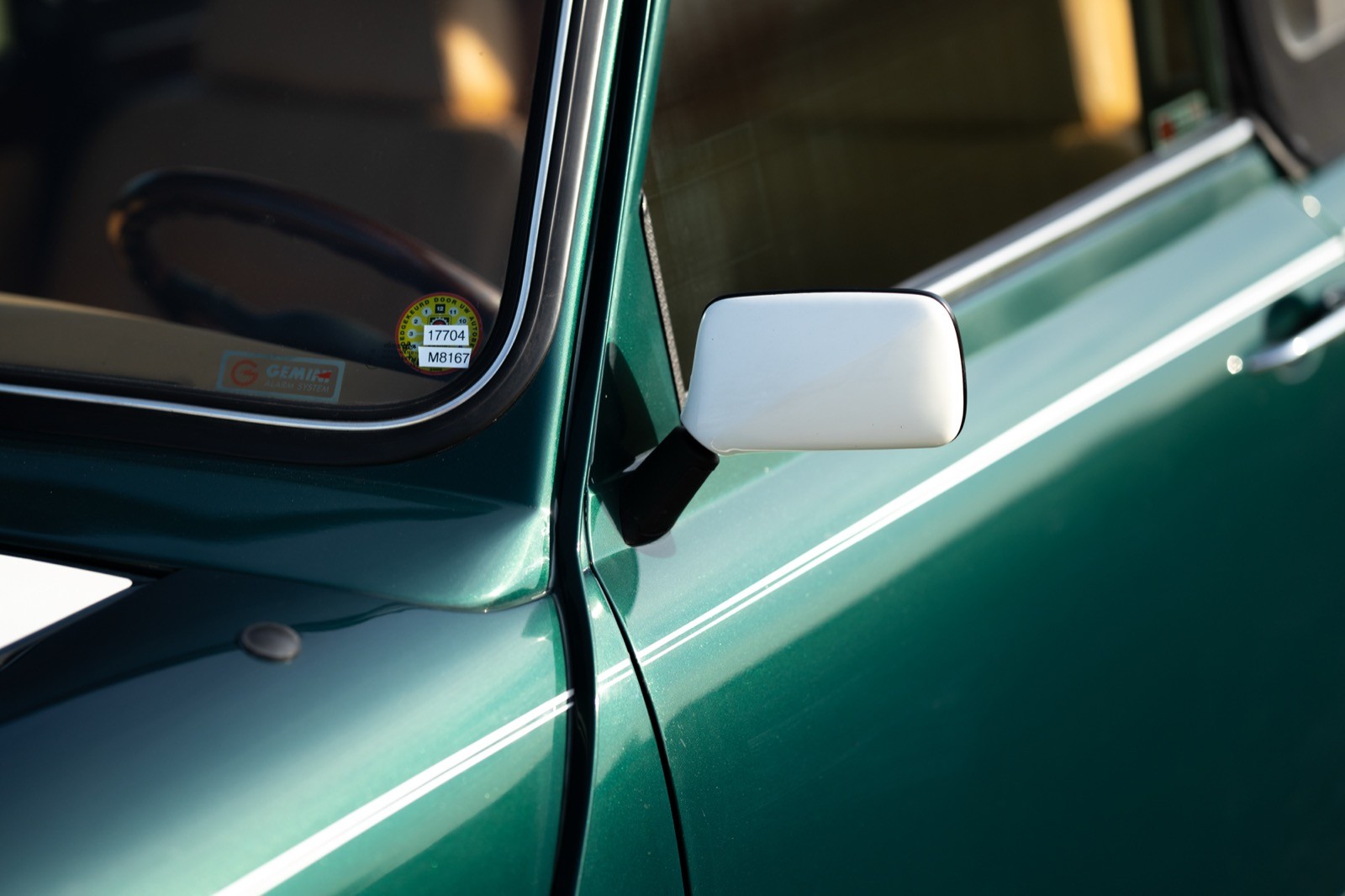 Close-up of a green car door with a side mirror and window, featuring reflections and highlights.