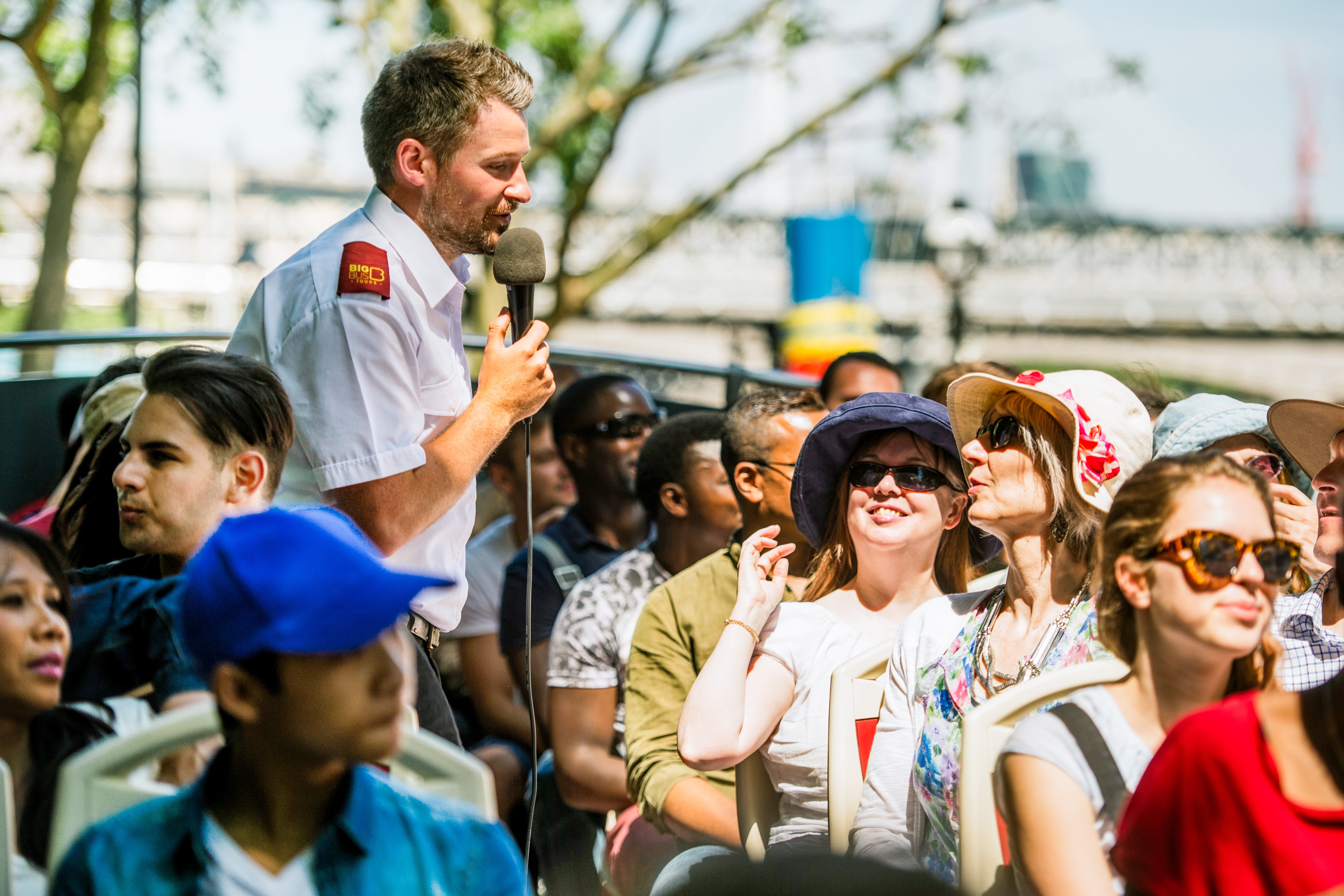 Turguide som snakker til passasjerer på en åpenbuss-sightseeingtur i en by.