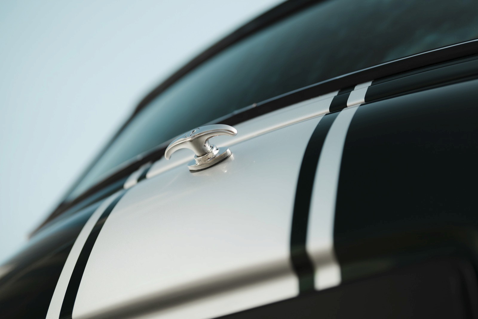 Close-up of a sleek car hood ornament with shiny metallic detailing against a soft blue background.
