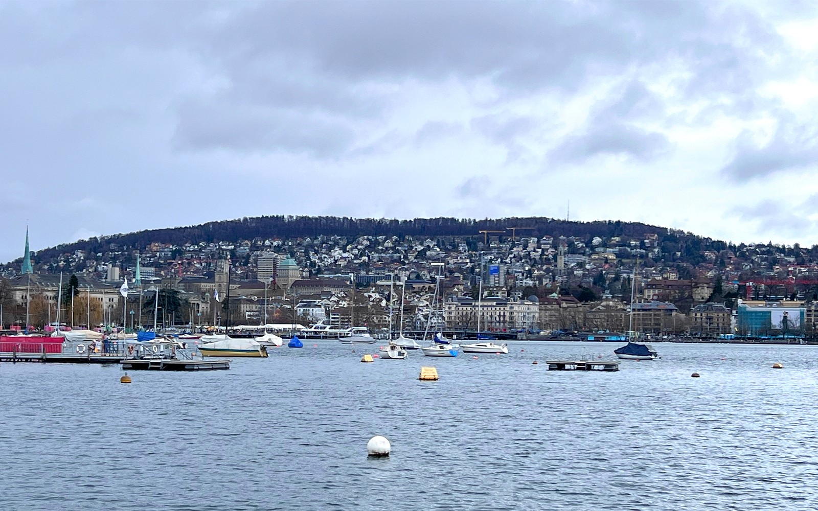 Båtar på Zürichsjön med stadssilhuett och kullar i bakgrunden, vy från sightseeingtur.