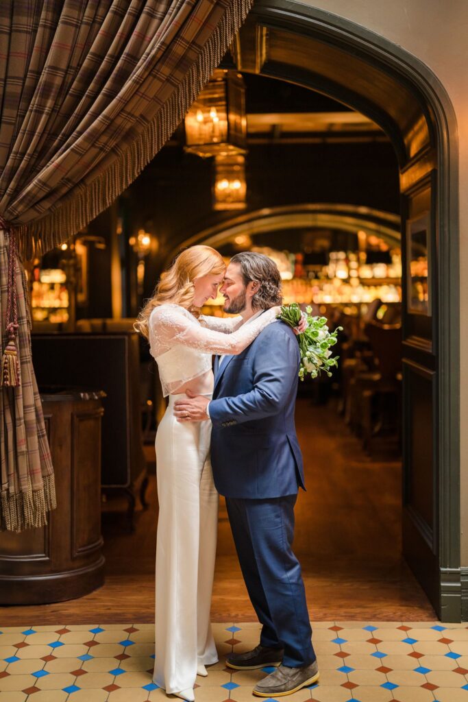 Wedding couple embracing beneath a dark wood archway beside a warmly lit bar