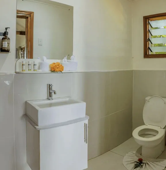 Spacious bathroom at Uprising Beach Resort, featuring a white sink, toilet, mirror, and a louvered window.