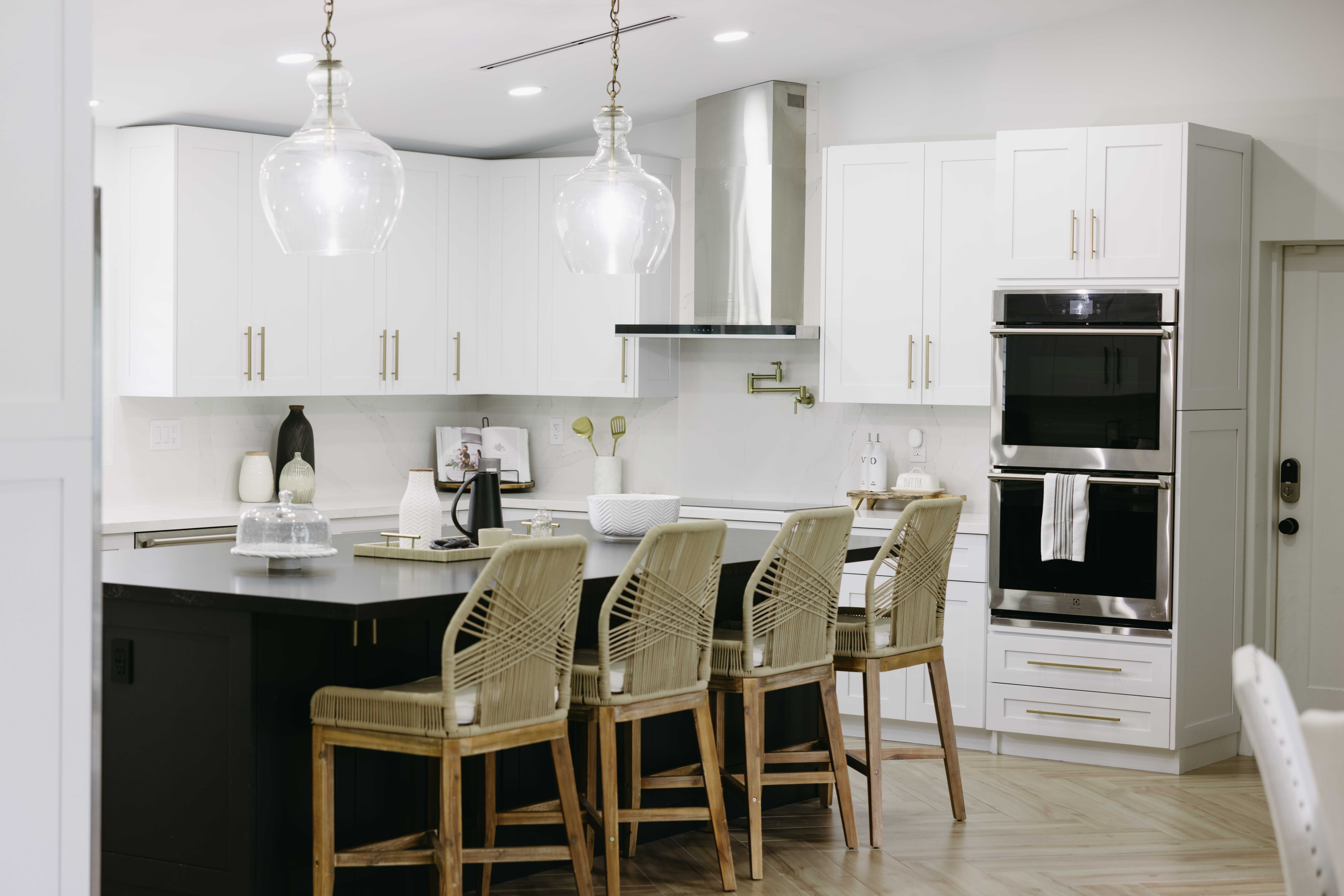 Modern kitchen with black island, white cabinets, stainless steel appliances, and bar stools.