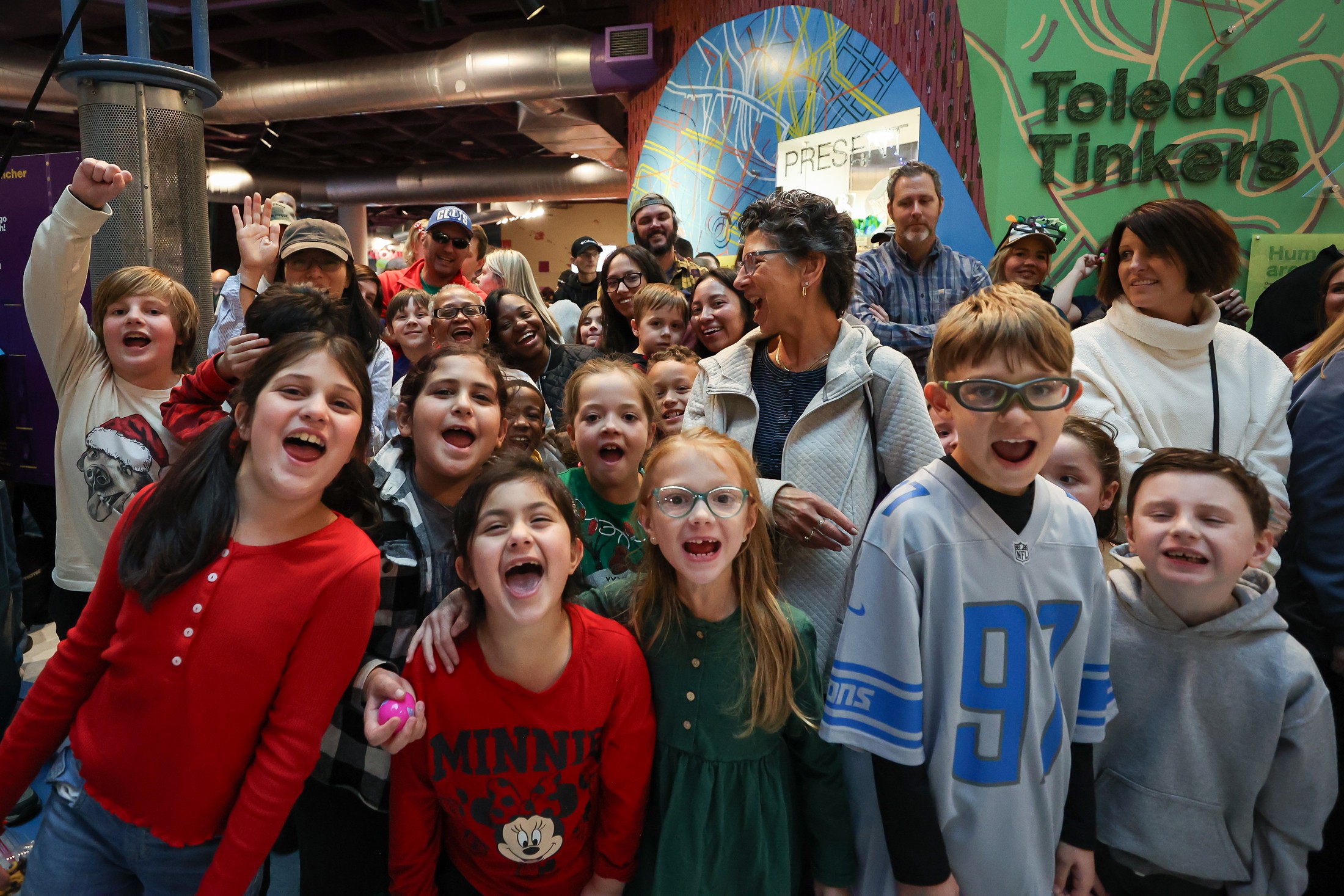A group of smiling, excited children look at the camera on a field trip.