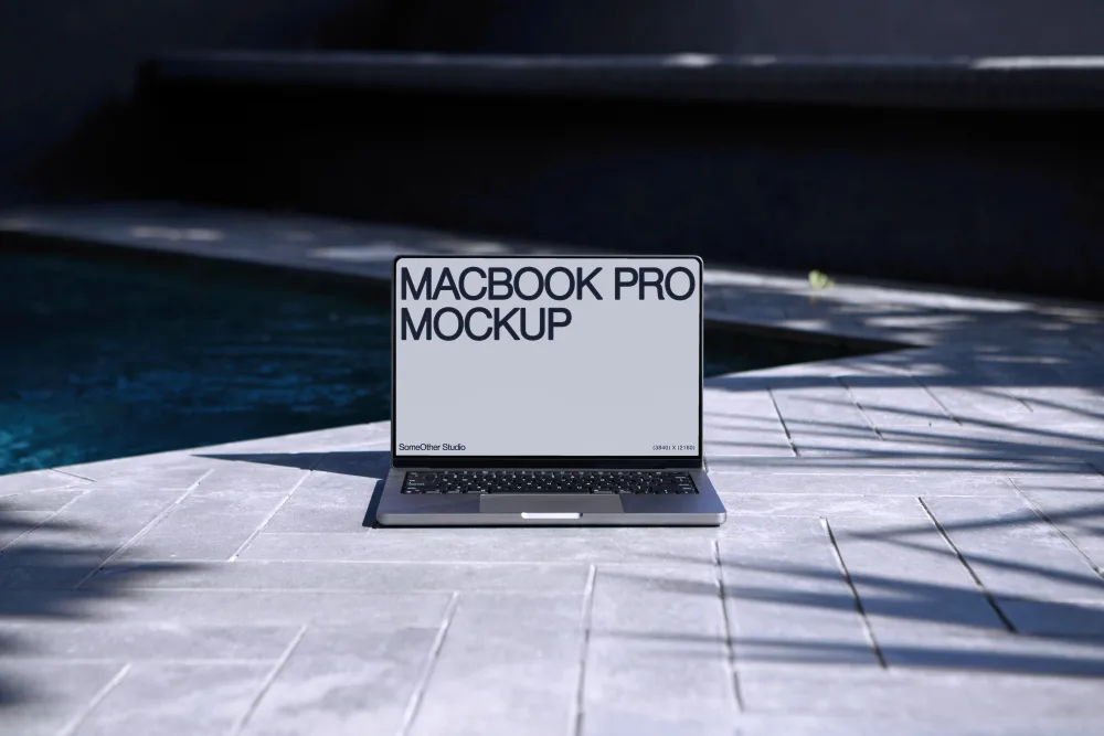 A MacBook Pro mockup on light gray poolside tiles, with dark blue water and shadows from surrounding foliage adding contrast in a serene outdoor setting.