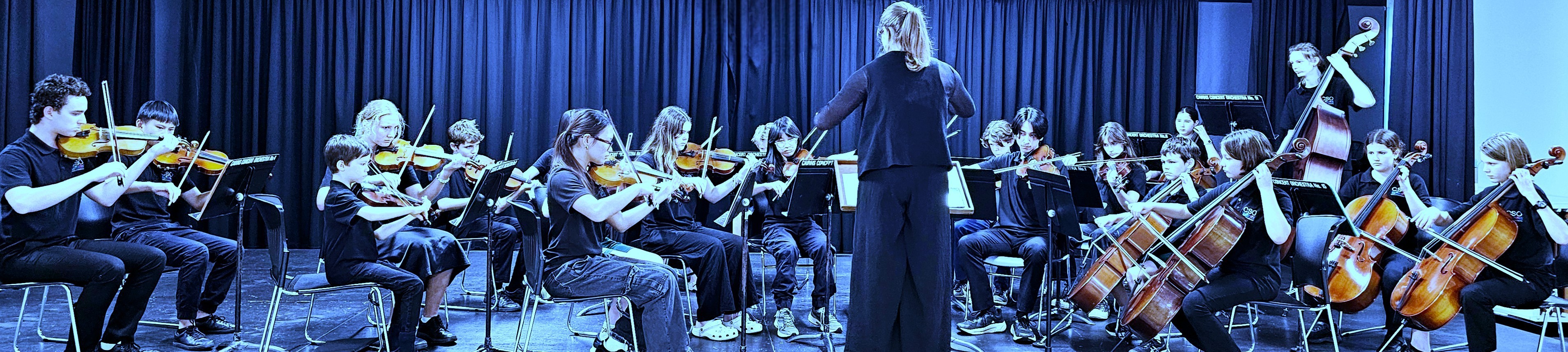 Cairns String Orchestra youth ensemble rehearsing under conductor's direction with violins, violas, and cellos in black and white