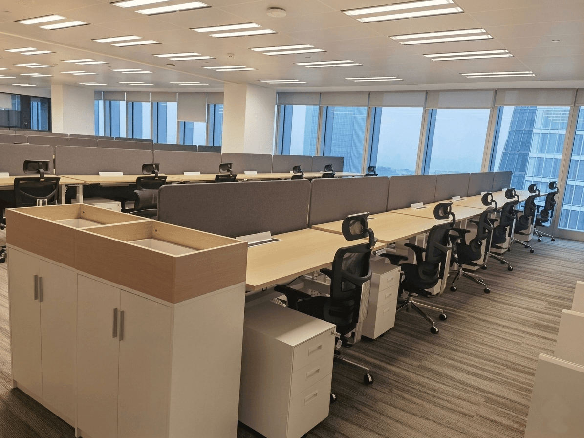 Modern open-plan office featuring rows of ergonomic A9 office chairs with mesh backs, light wood desks with grey privacy dividers, and white mobile pedestal filing cabinets.