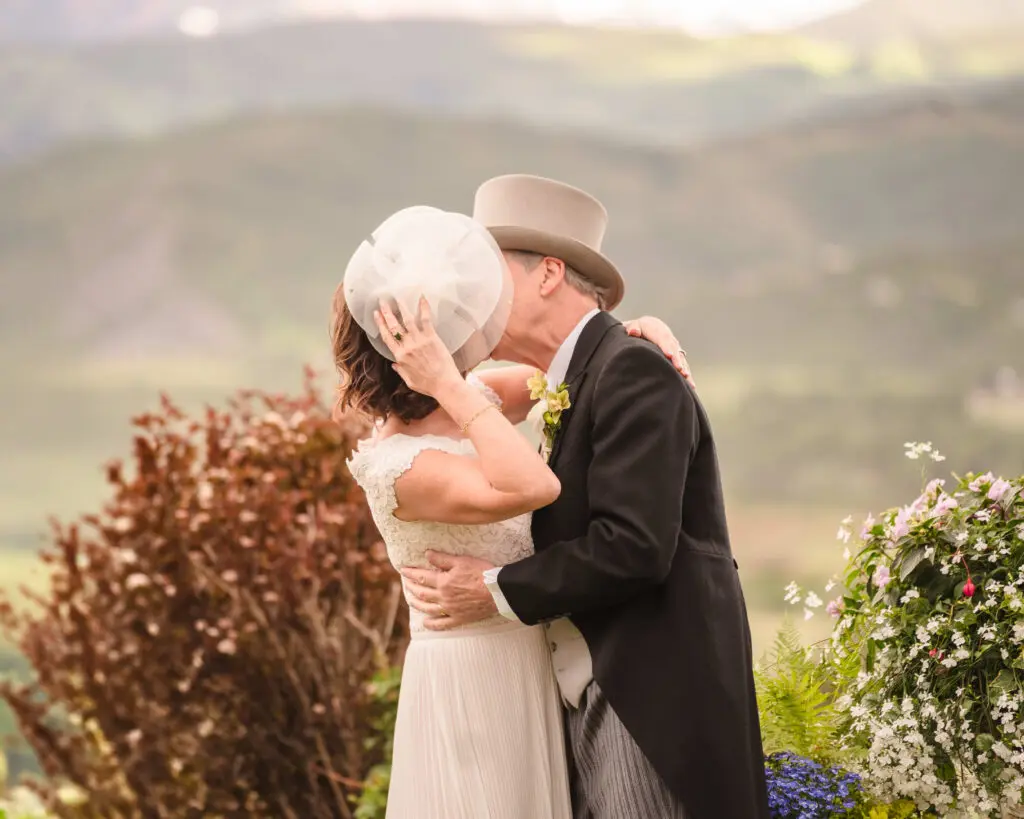The bride and groom sharing a kiss during their outdoor ceremony, surrounded by lush greenery and mountain views at their Chaparral Ranch Wedding.