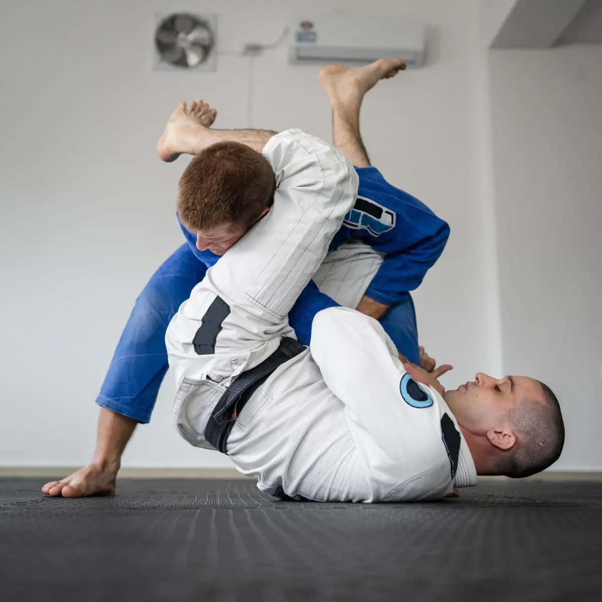 Two adults practicing Brazilian Jiu Jitsu ground techniques during training