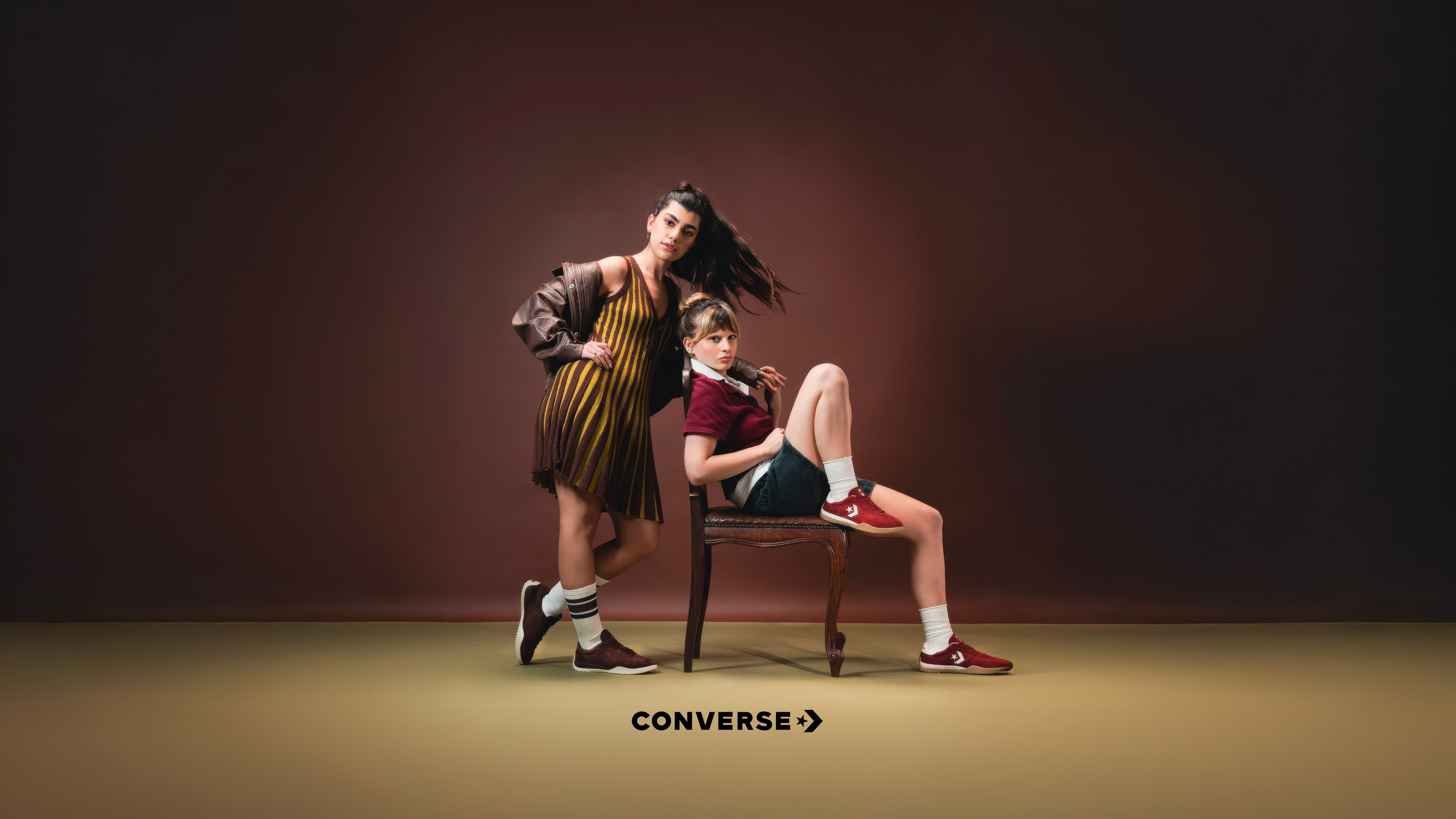 Person in yellow jacket and orange pants sitting on a blue chair, yellow background