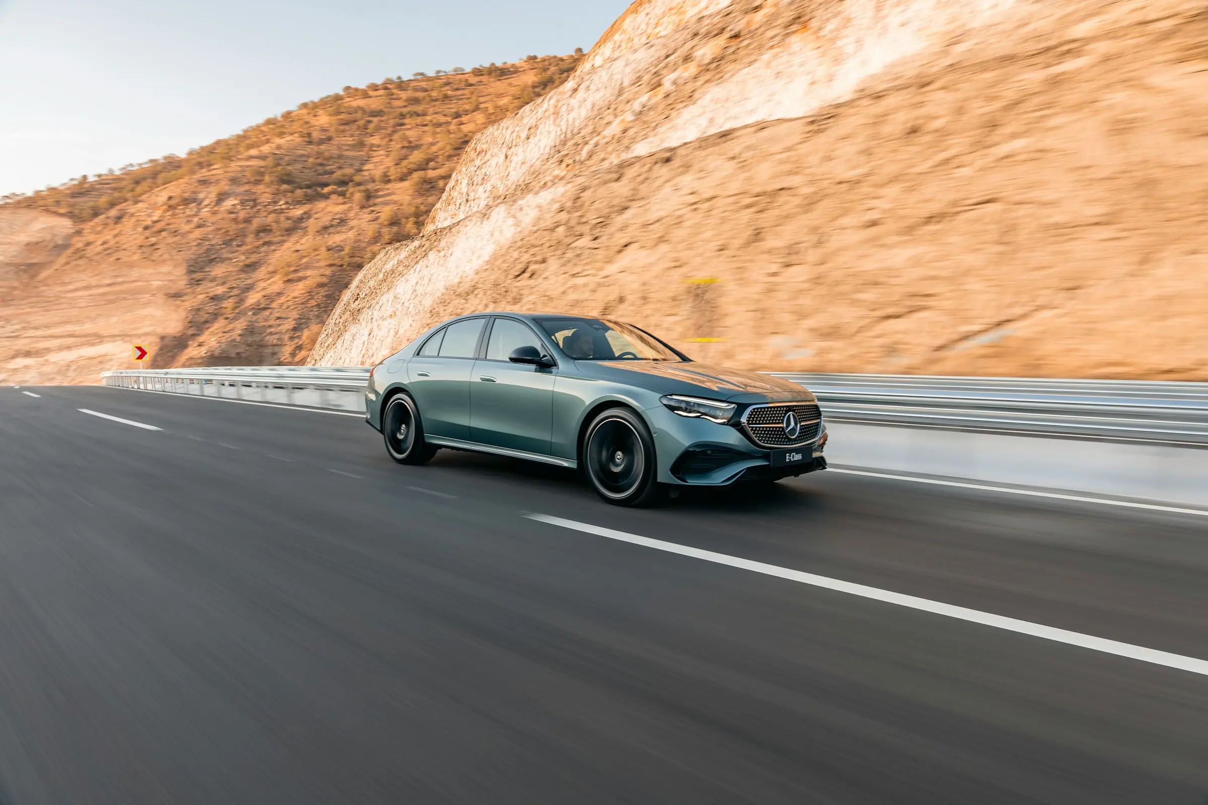Mercedes-Benz sedan driving on a highway through rocky hills during daylight
