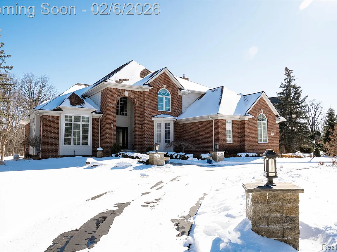 A modern brick house with a two-car garage, well-manicured lawn, and clear blue sky in the background.