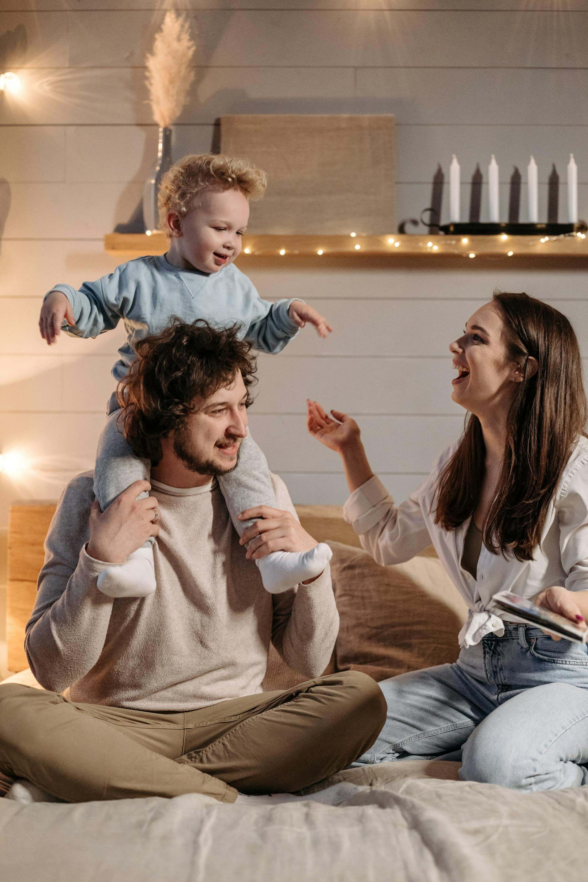 A happy family sits on a bed, using a laptop while their baby plays nearby, creating a cozy and joyful atmosphere