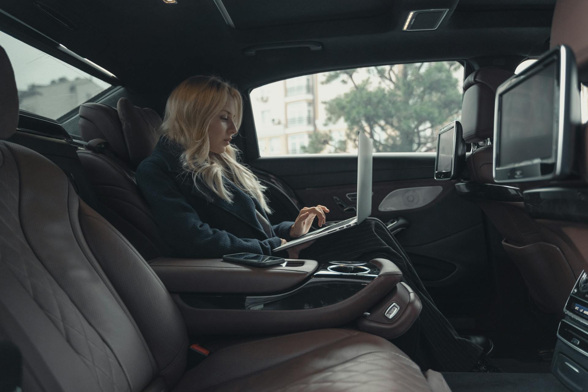Woman working on a laptop in a luxury car interior, showcasing executive amenities for corporate transportation.