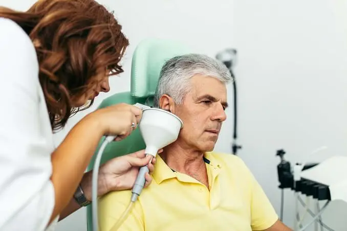 A healthcare professional attends to an elderly man sitting in a chair, looking concerned during a consultation.