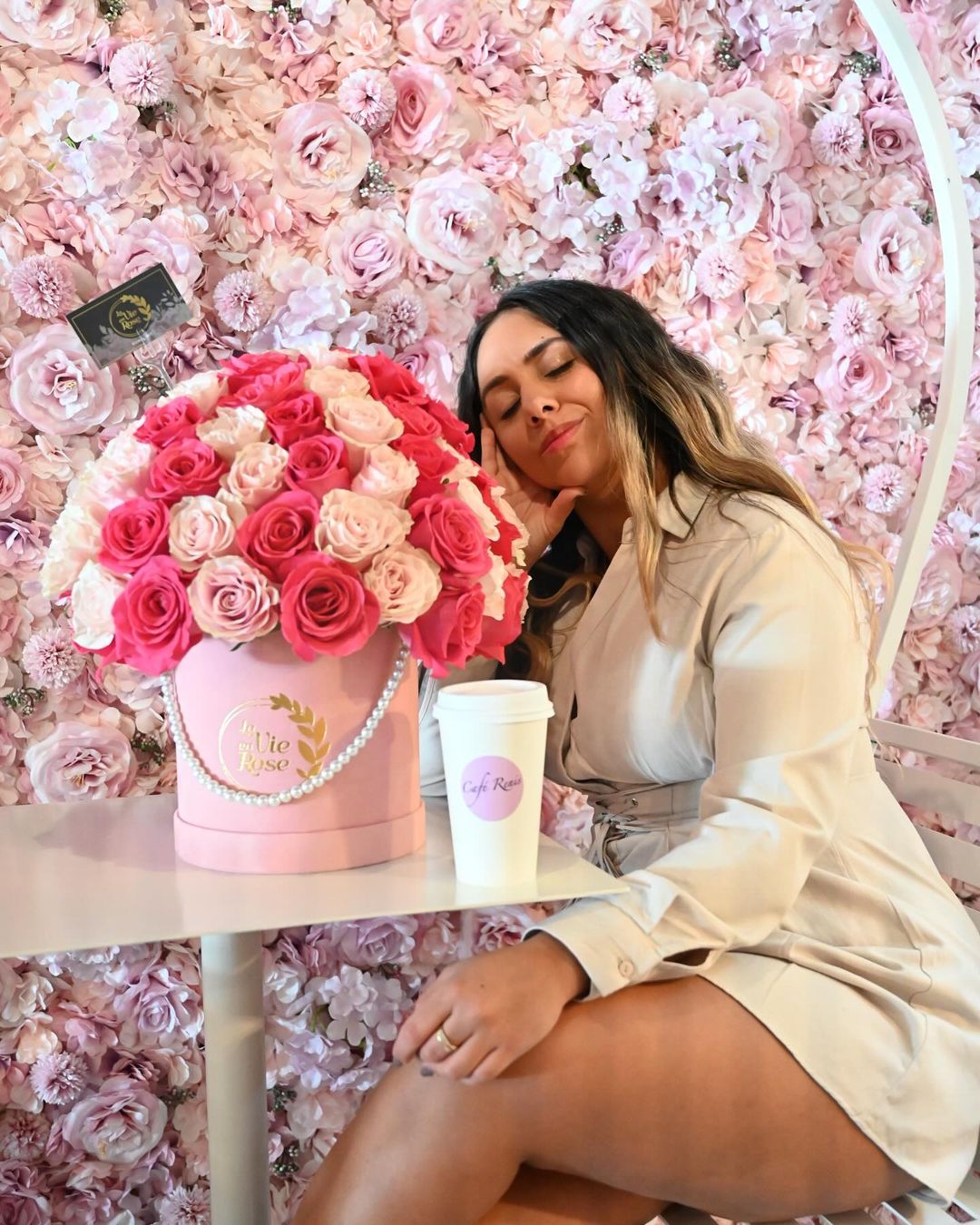 A girl sitting at Cafe Renis in front of a rose flower wall