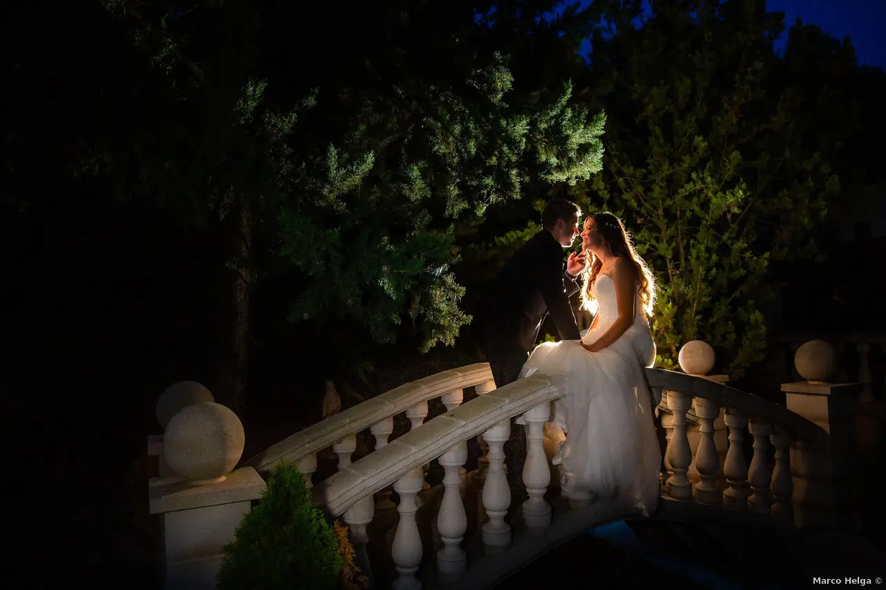 A group of people gather outside a rustic stone building surrounded by lush greenery and flowering plants, bathed in warm, natural sunlight, capturing a serene and welcoming ambiance.