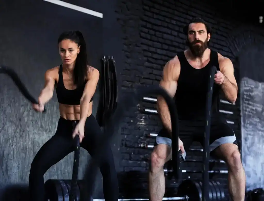 Two athletes performing battle rope training in a commercial gym