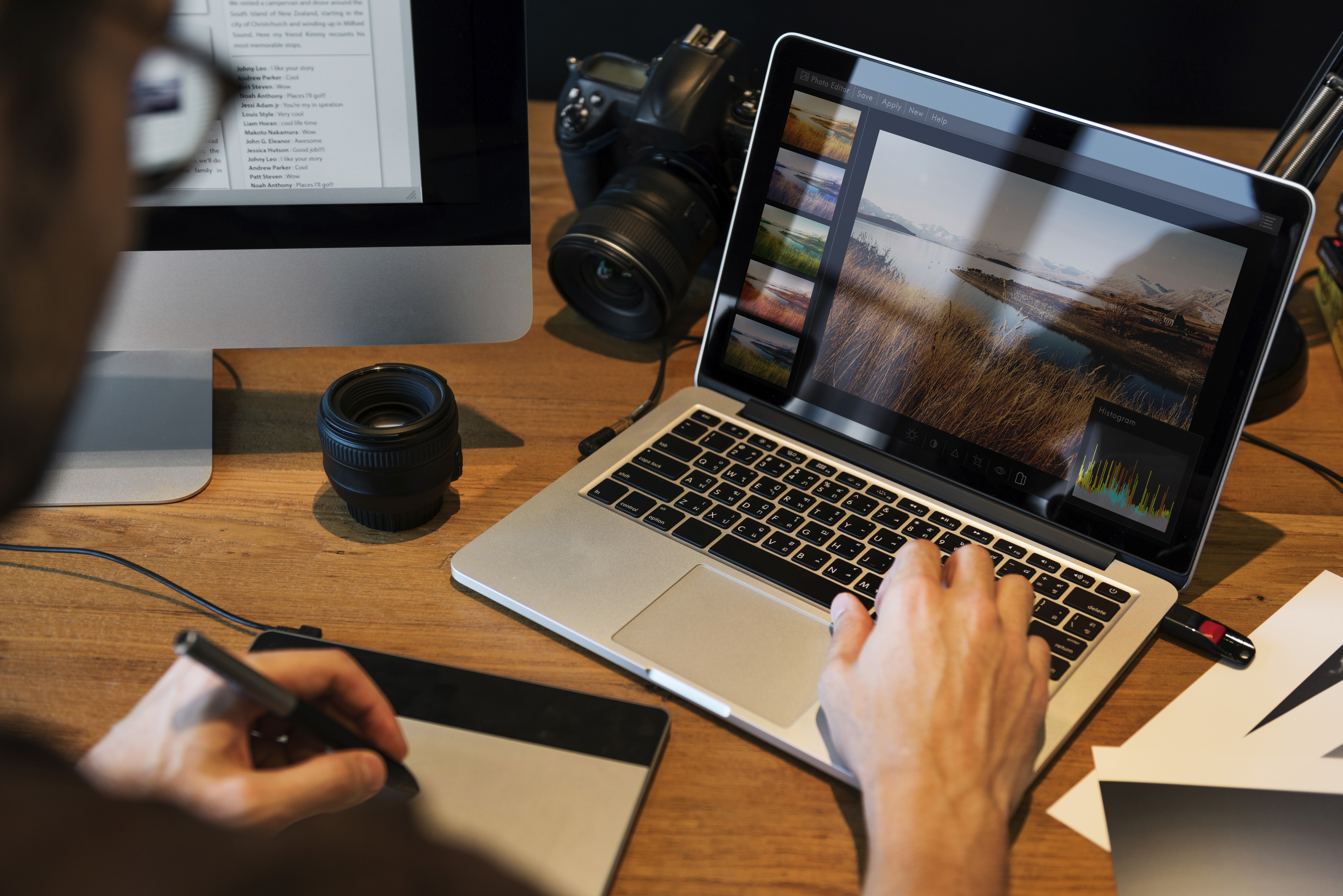 Creative professional editing a landscape photo on a laptop using photo editing software and a graphics tablet, with a DSLR camera and lens on a wooden desk