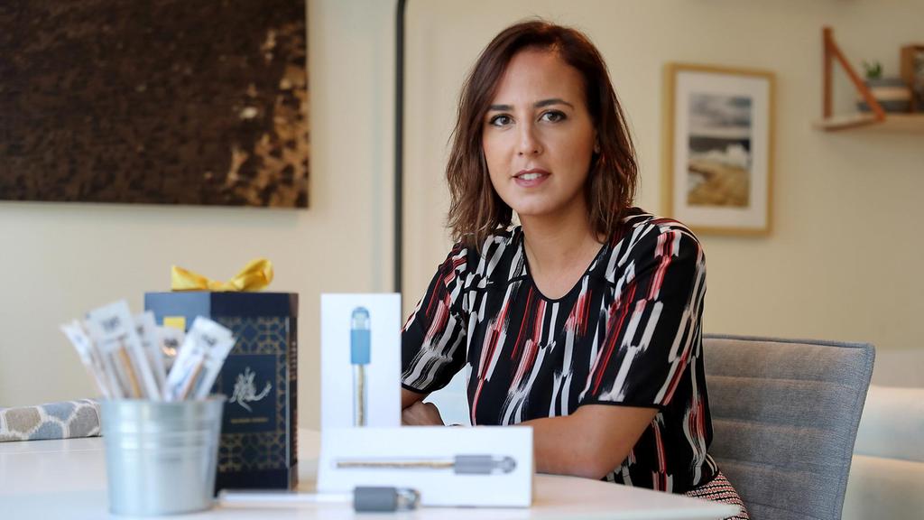 A photo of a woman sitting at a table. On it there are a few boxes and a pencil holder. On the boxes there are images of pencils.