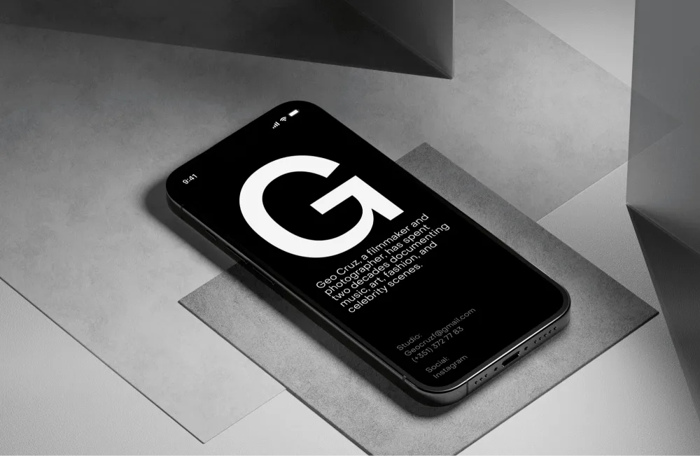 A modern smartphone with a black display showcasing a bold white letter "G" and minimal text, resting on layered gray textured surfaces with sharp angles, creating a contemporary and sleek aesthetic.