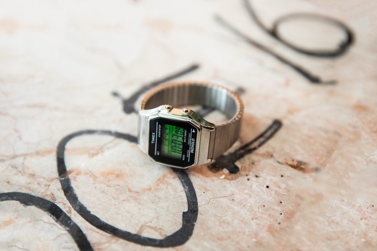 Metal digital wristwatch on a stone surface with small hand tools nearby.