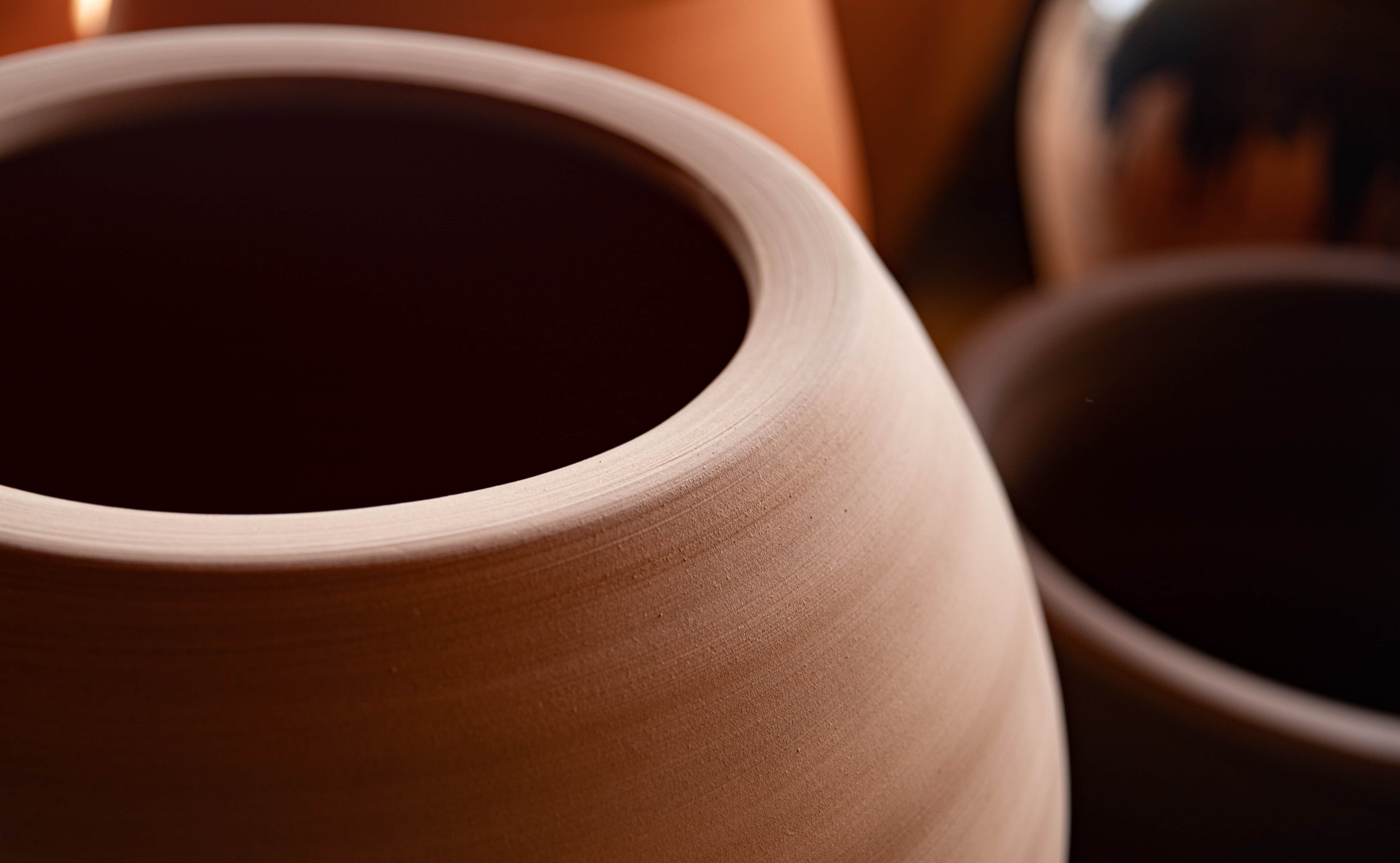 Close-up photo of raw, unglazed terracotta pot rims showing the earthy texture and concentric hand-spun lines.