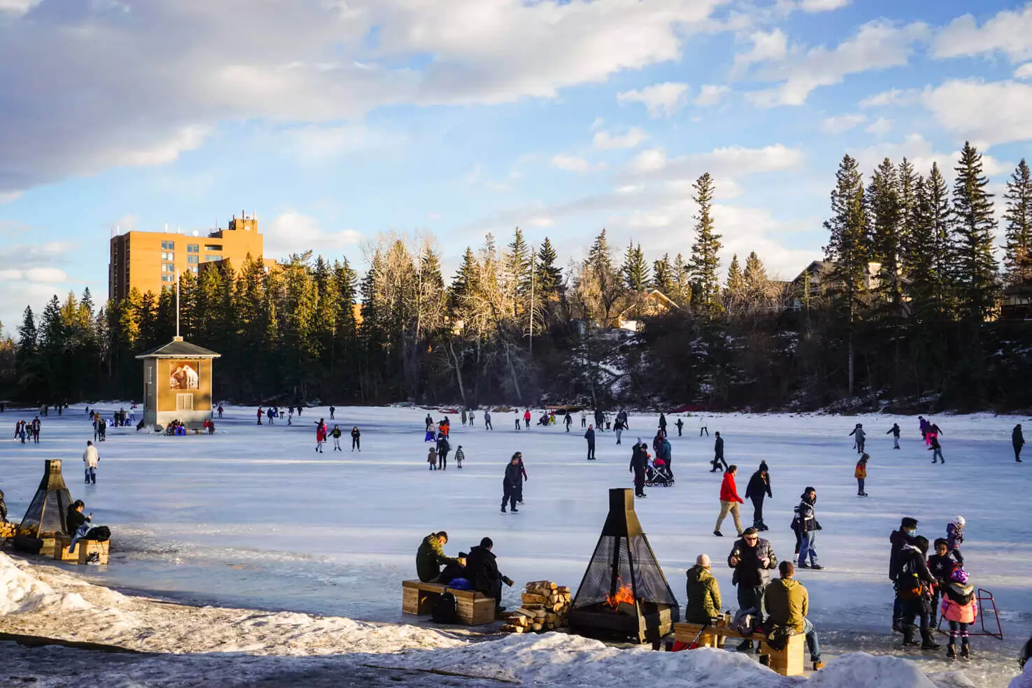 People ice skating on a frozen lagoon near outdoor fire pits at Bowness Park in Calgary
