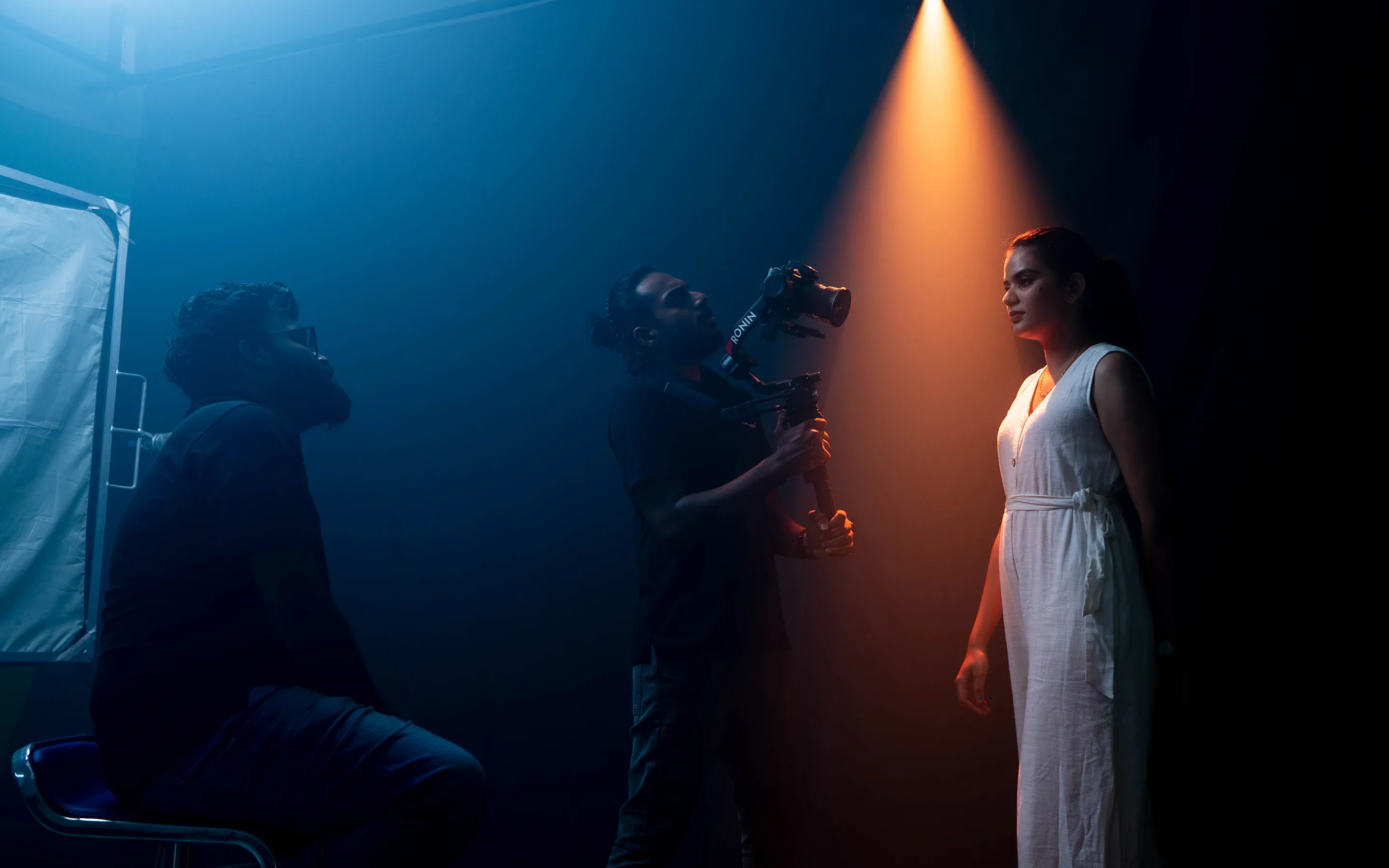 Woman under spotlight during videography shoot as crew films and monitors lighting in studio