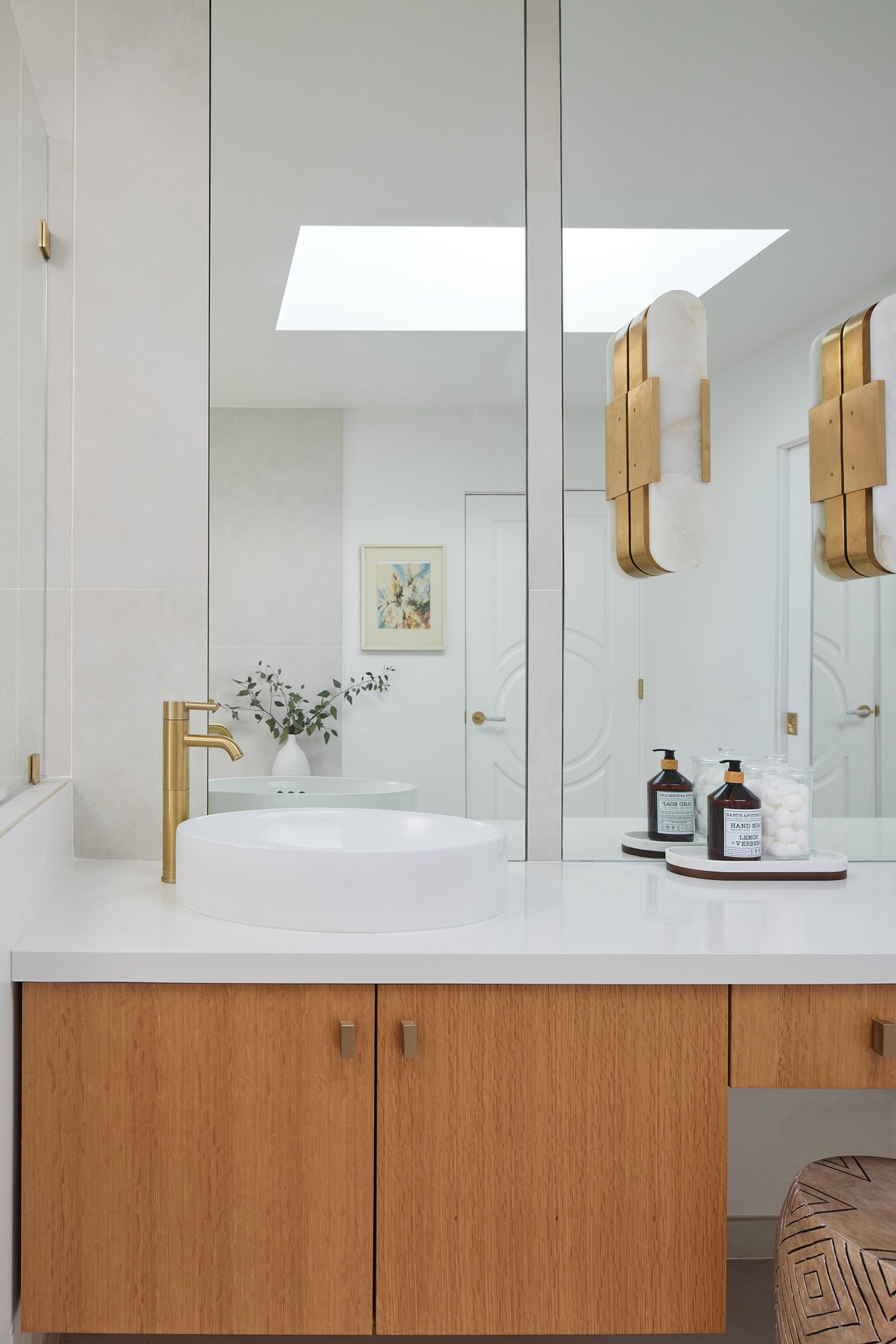 Bright master bathroom vanity with a white quartz countertop, mounted stone light fixtures, bronze fixtures, vertical grained flat panel cabinetry, with built in vanity space by Jubilee Interiors in Los Angeles, California