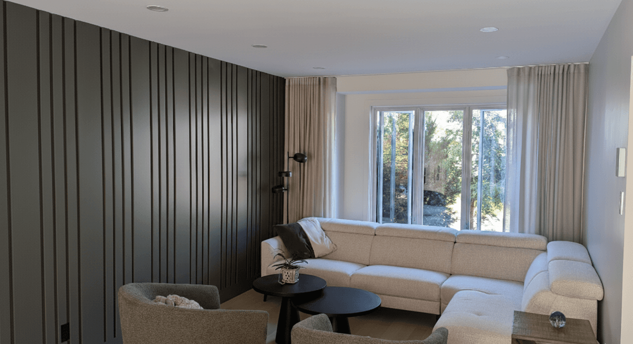 Salon magnifiquement agencé. Tons de beige et de vert. Habillage de fenêtre du plafond au plancher. Moulures vertes sur le mur de gauche pour un accent incroyable. Luminaire sur pied noir au fond, à côté du divan en L de couleur crème. Deux tables basses rondes et noires apportent du dynamisme et du caractère. Table d'appoint en, parfaitement aassortie aux couleurs chaudes. Deux fauteuils vert olive complètement l'ensemble avec élégance.