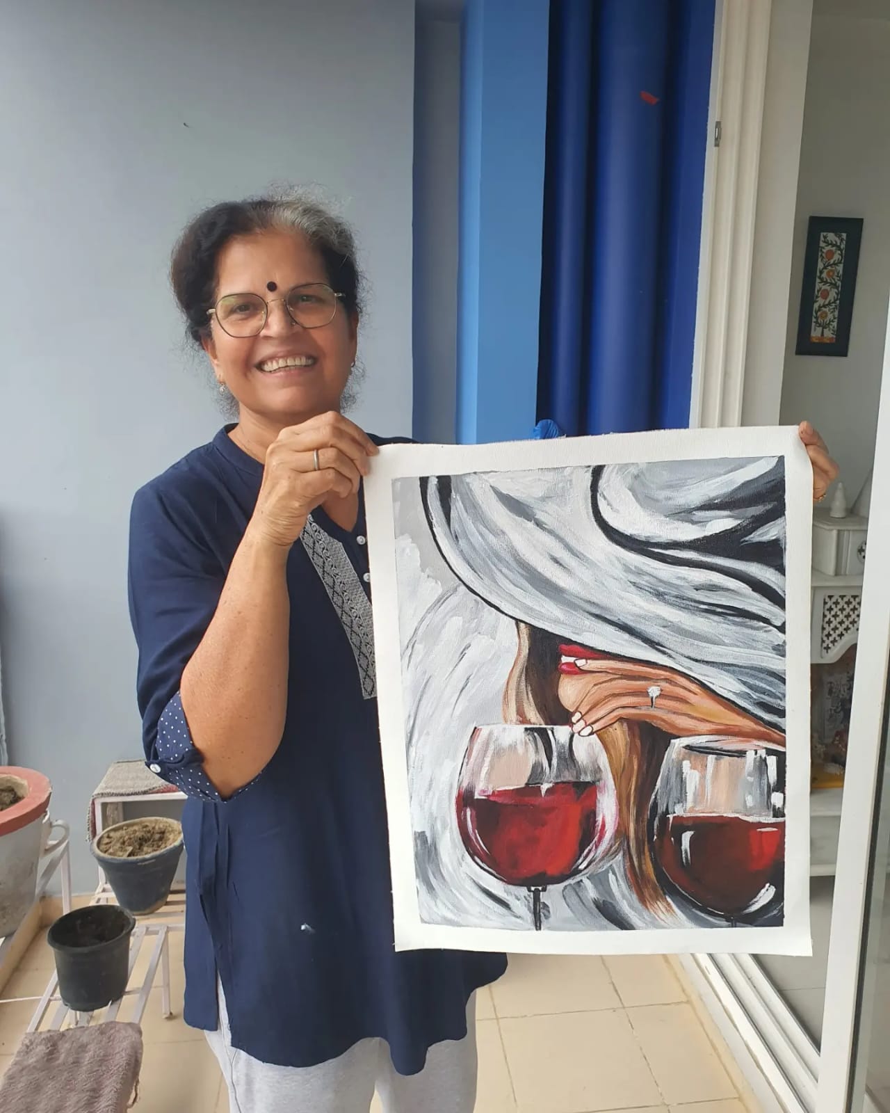 Creative Pod student holding an abstract painting of wine glasses made with poster colors on the balcony of The Creative Pod studio.