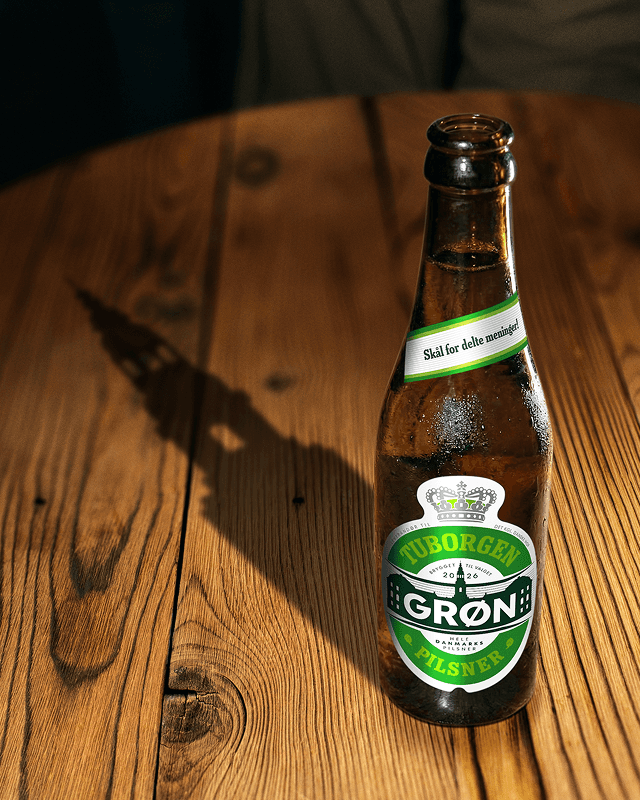 Tuborgen Grøn beer bottle on wooden table casting a parliament tower shadow, Tuborg x Borgen campaign 2026