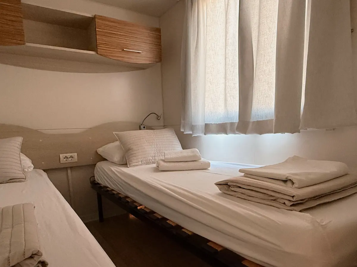 Spavaća soba mobilne kućice Dvije Suze 1 s dva odvojena kreveta i prozorom s laganim zavjesama
