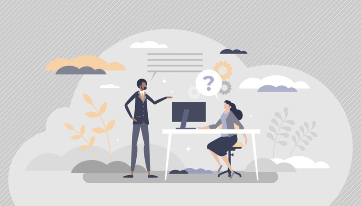 Illustration of two professionals in a tech-focused office setting, one seated at a computer and the other standing and gesturing—representing thoughtful, technical questions that demonstrate insight during IT interviews.