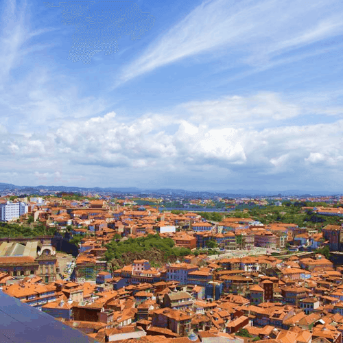 Aerial view of a cityscape with red-tiled buildings under a blue sky with scattered clouds.
