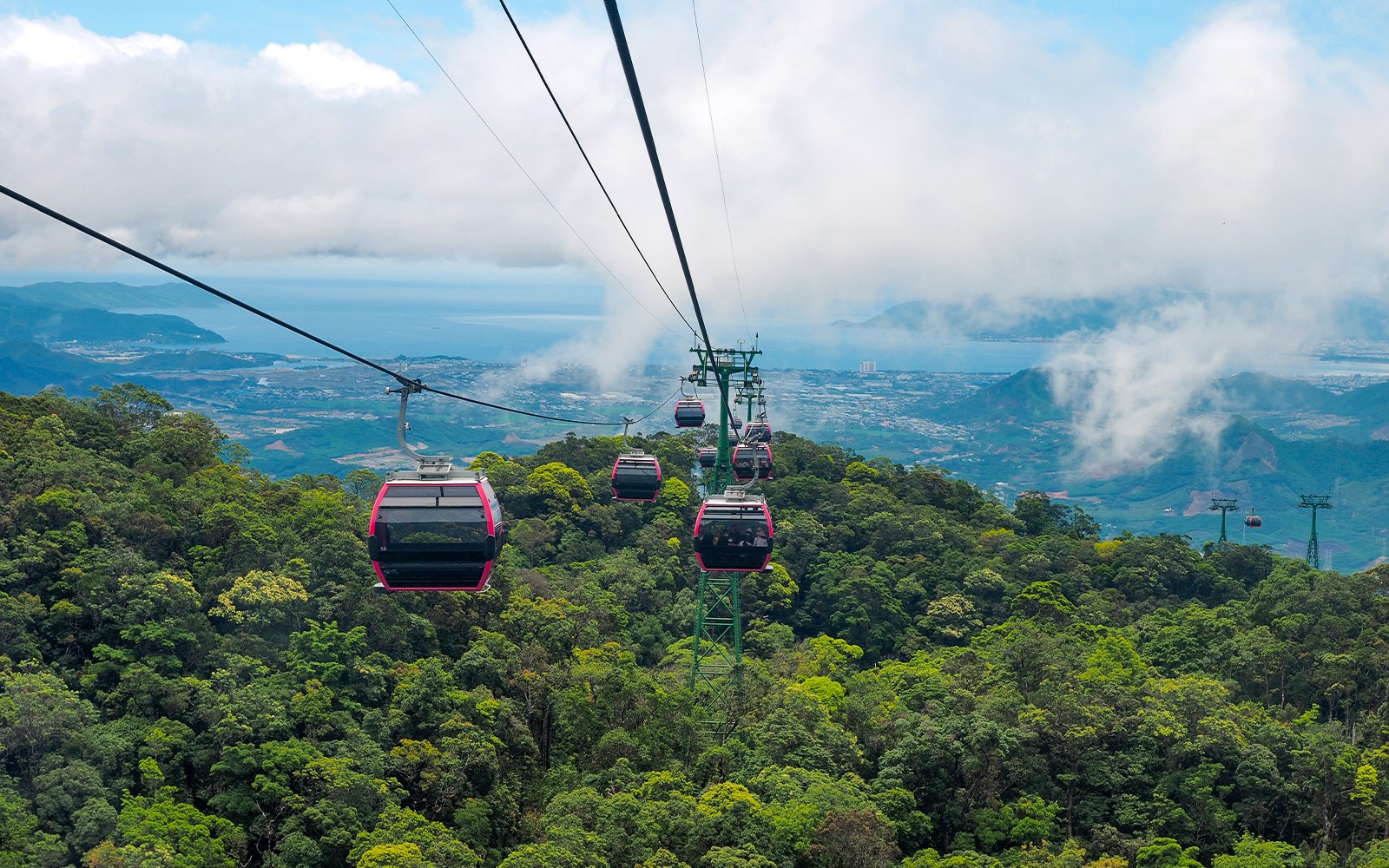 Cable cars over lush forest in Ba Na Hills, Vietnam, with distant city and ocean views.