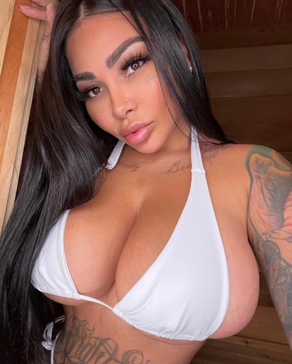 Mujer con vestido negro ajustado y escote pronunciado, posando en un ambiente iluminado con luz púrpura.