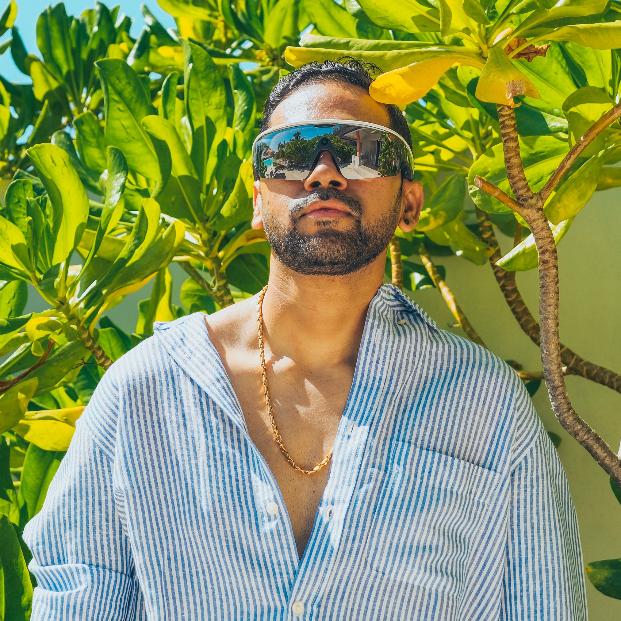 Close-up of a person wearing white triangle sunglasses on a teal background.