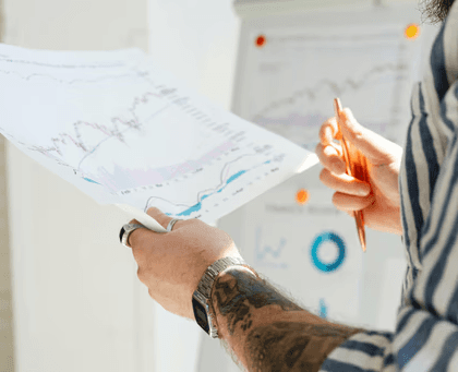 Person reviewing financial charts and graphs on paper with a pen in hand.