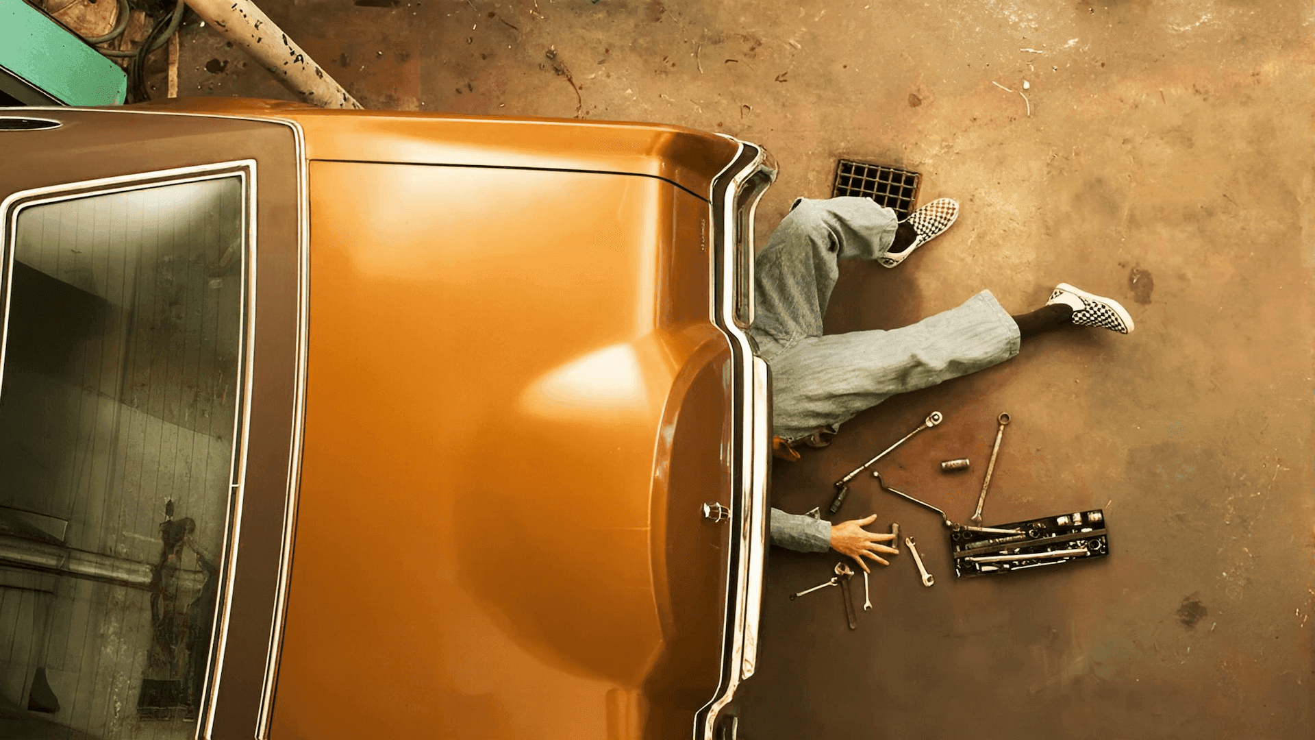 Mechanic working under vintage car with scattered tools—representing unseen engineering effort.