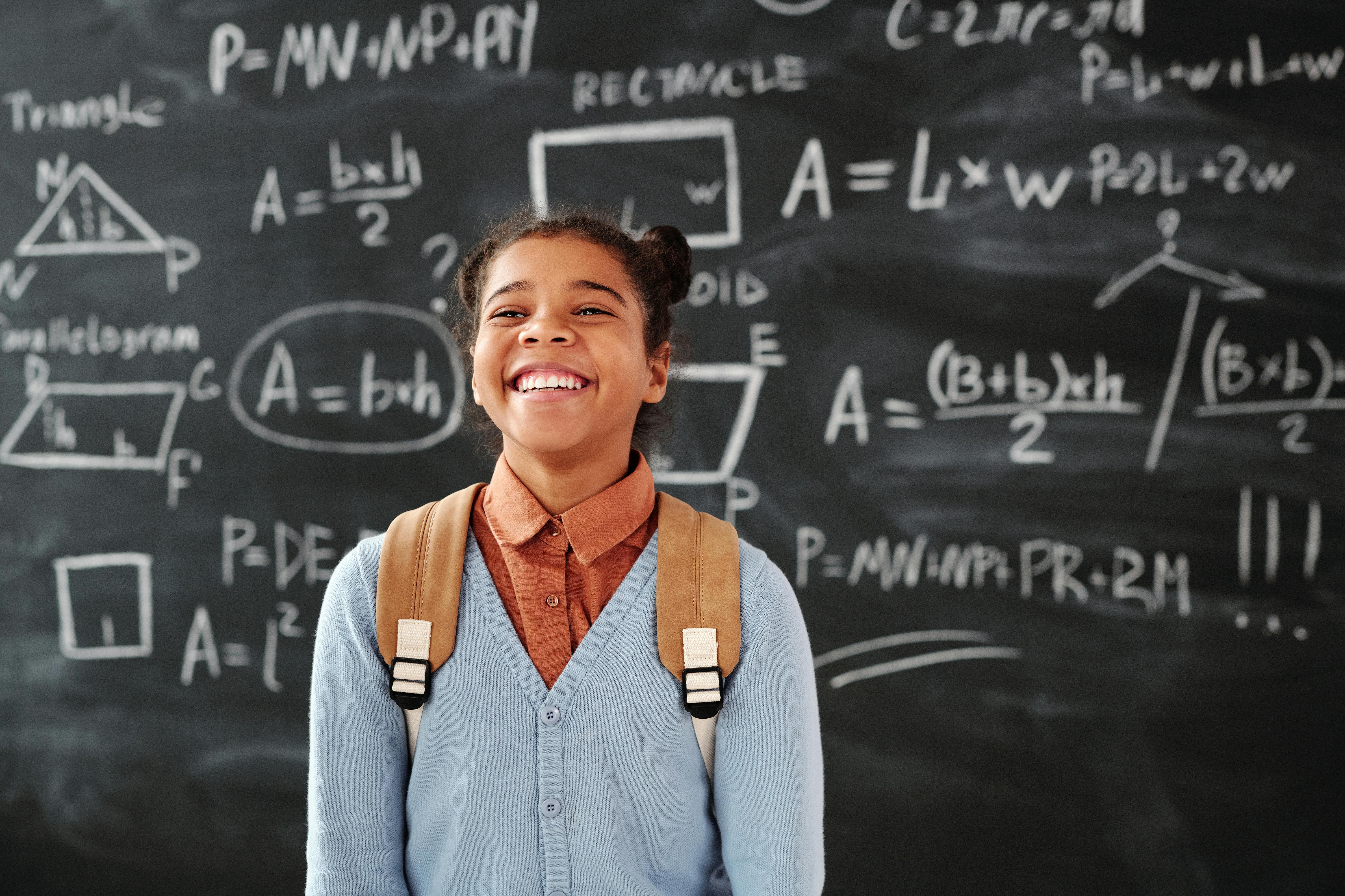 Smiling student in front of math formulas on chalkboard representing innovative ideas using AI for personalized learning and problem-solving