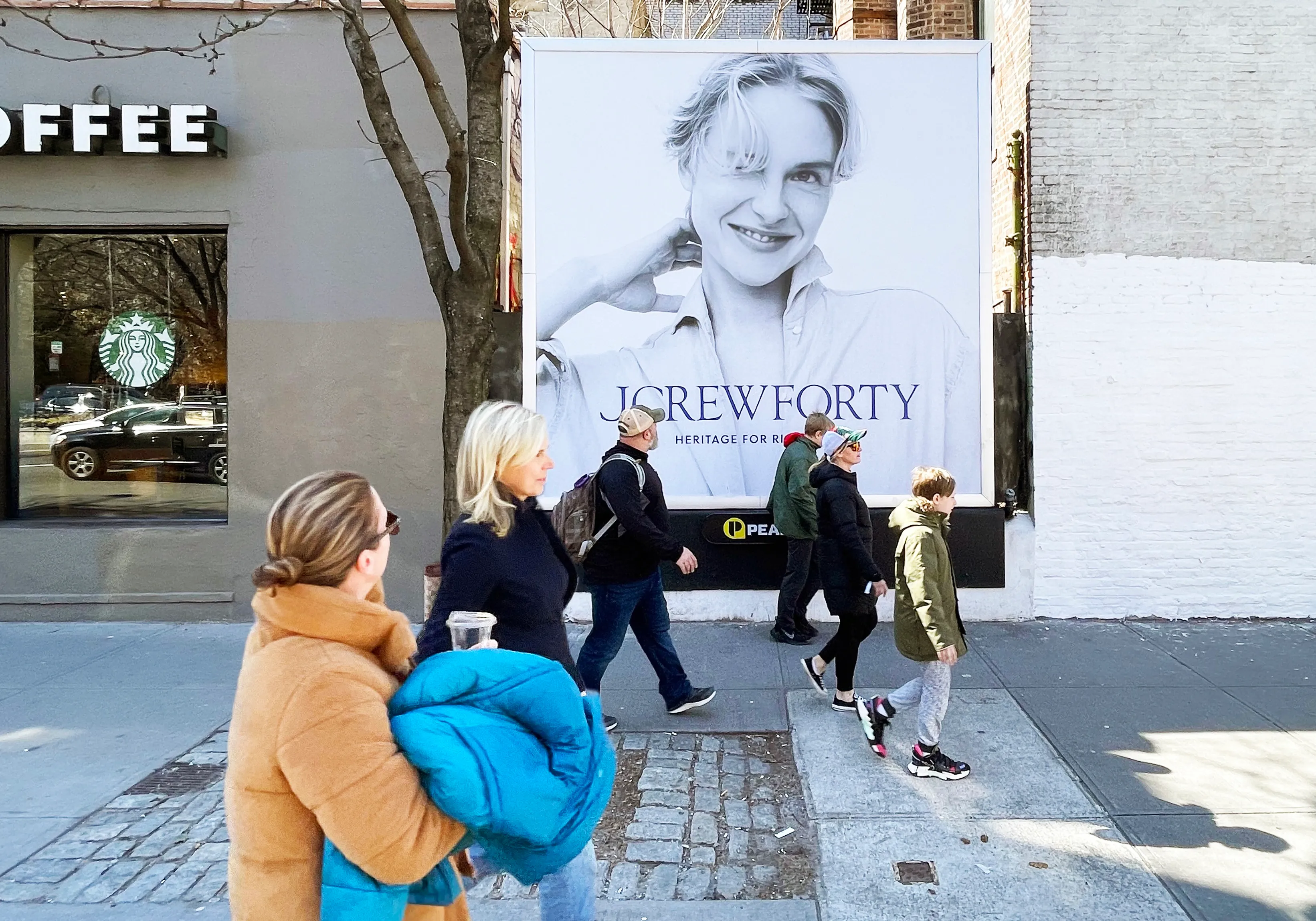 a man walking down a street past a large poster