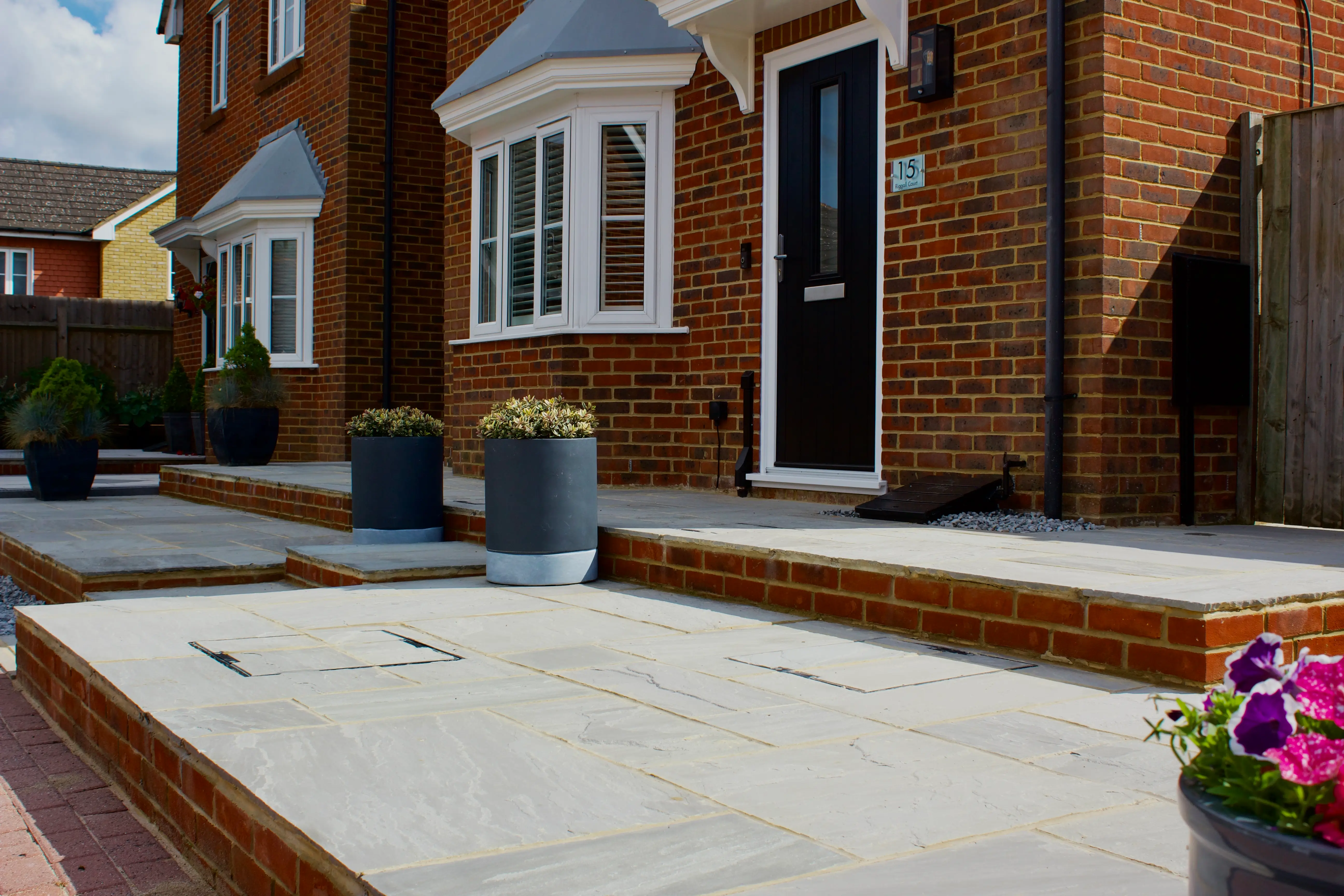 A well-designed entrance with stone steps, a porch, and flower pots beside a brick building.