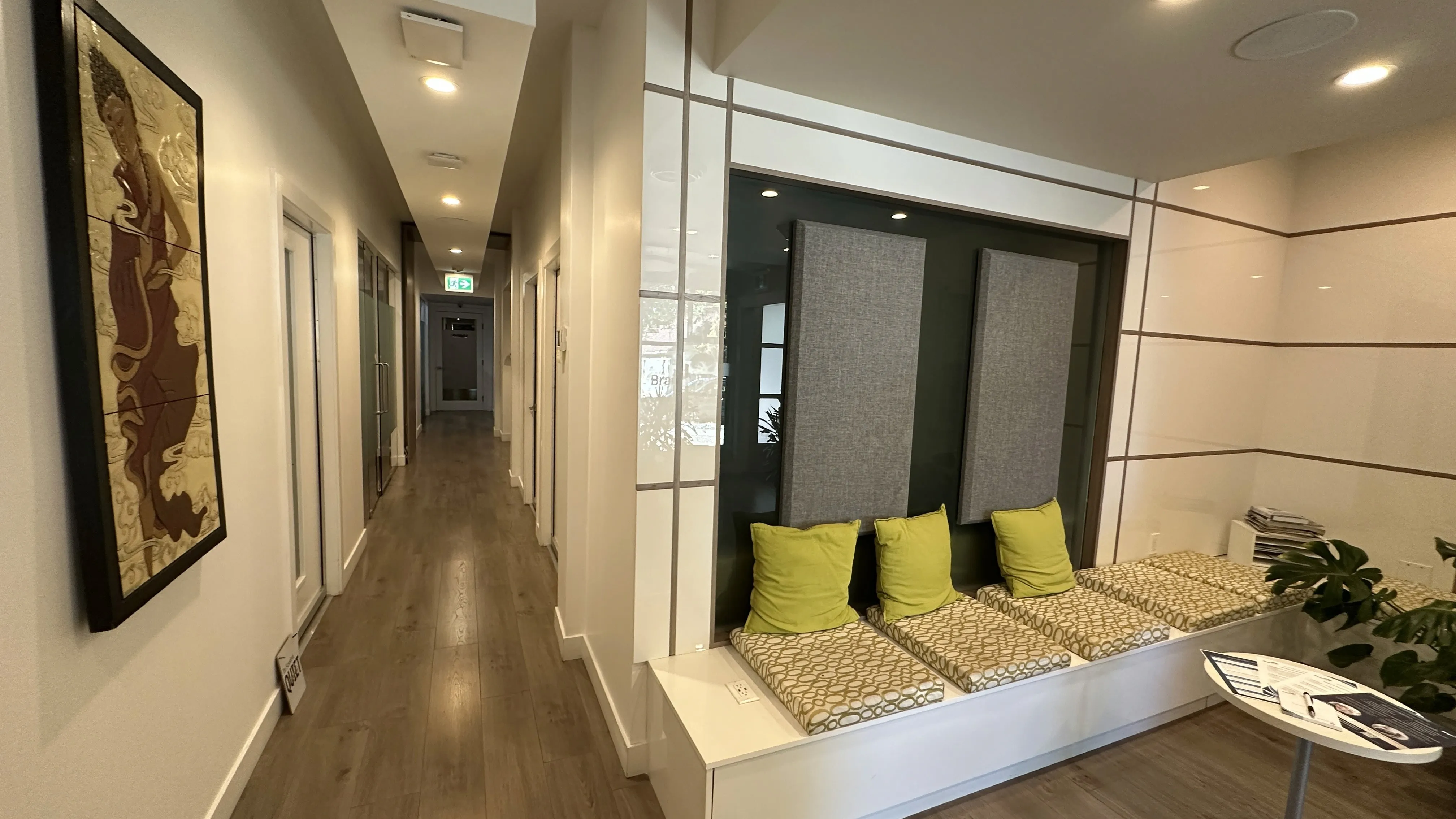 Hallway with built-in acoustic panel bench seating, green cushions, and wall artwork