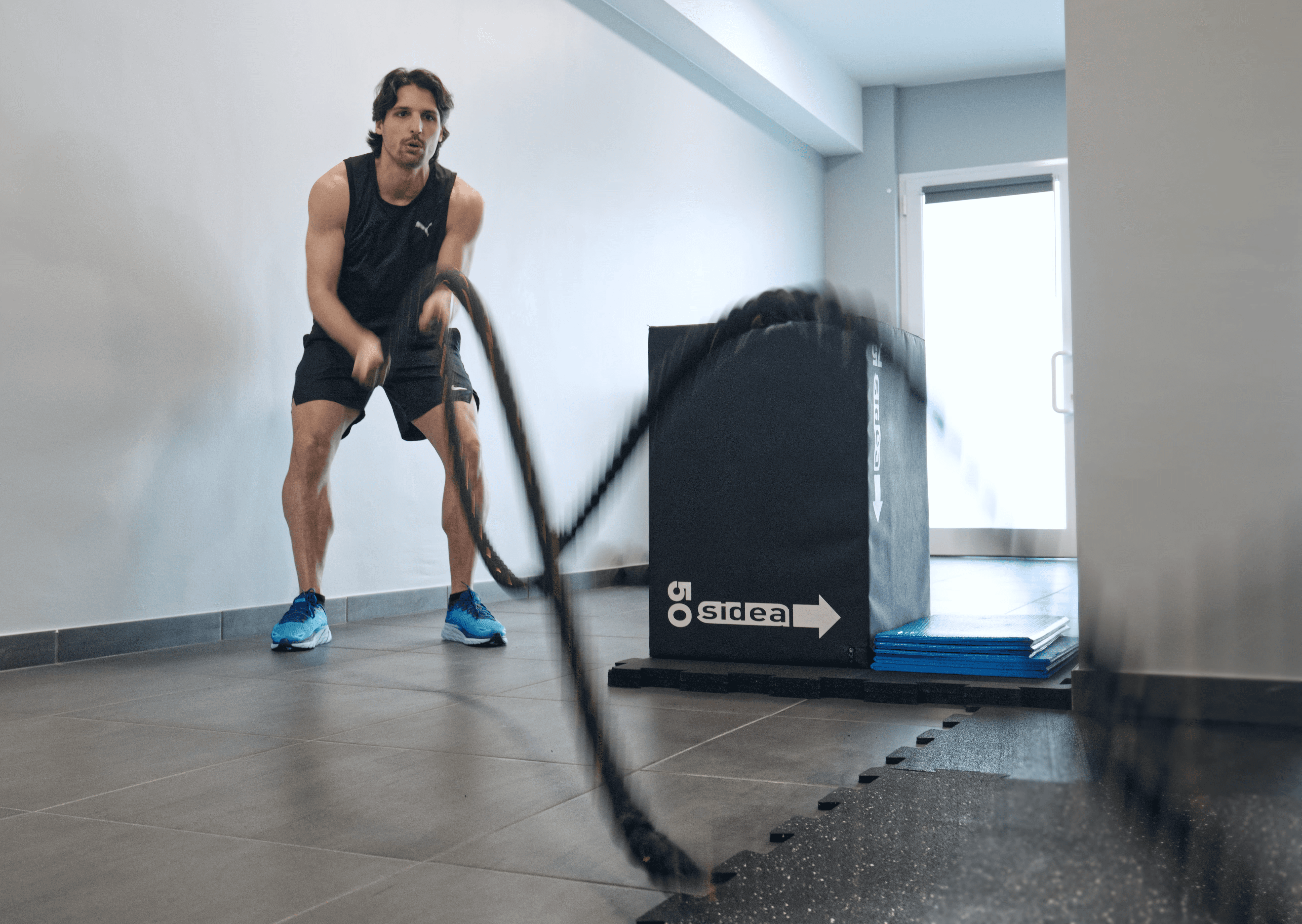 A person in a white outfit sits on a round stool in a spacious, minimalist room. The wall is covered with framed photos surrounding a large screen, creating a serene, contemplative atmosphere