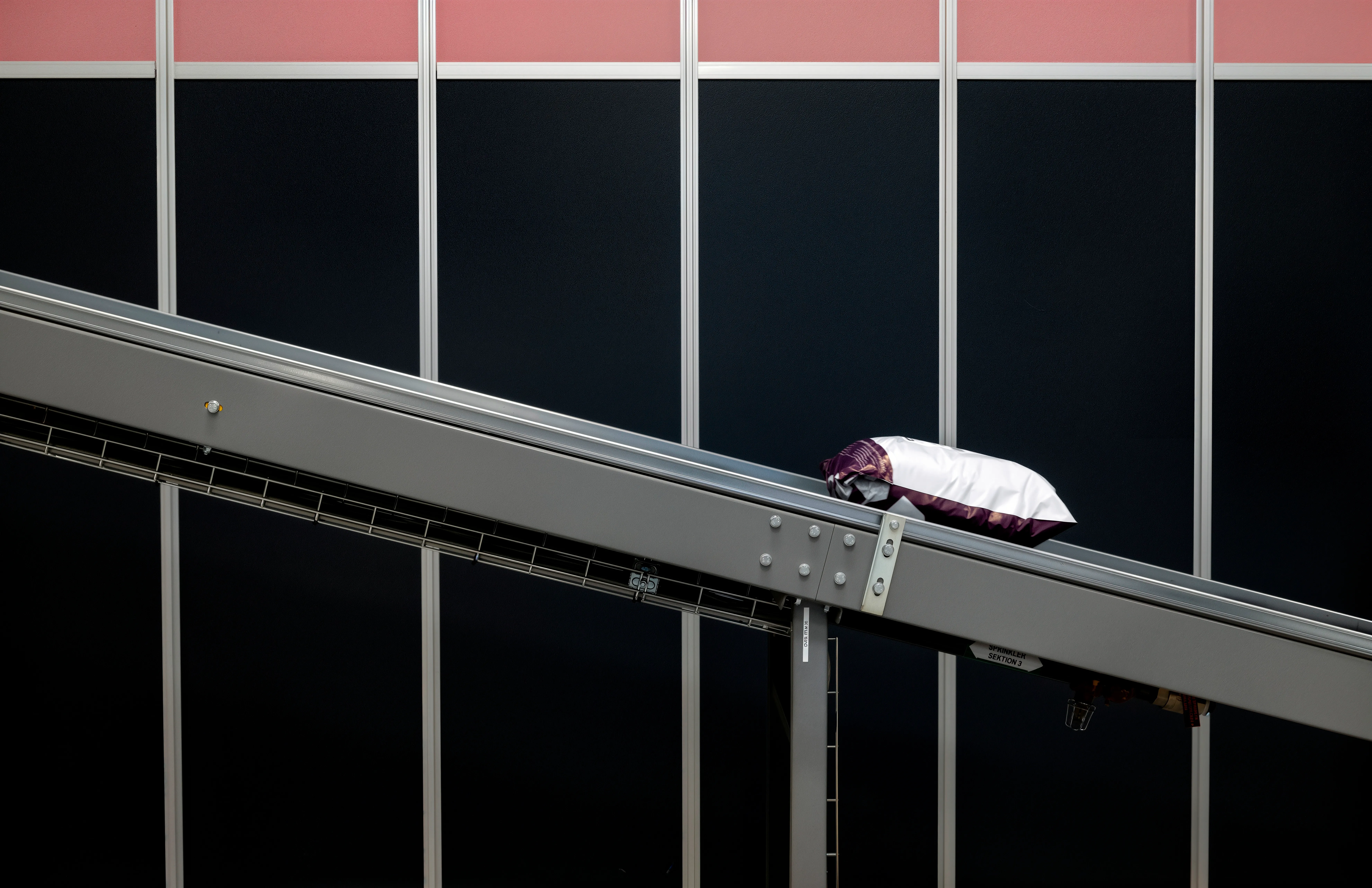 Paket på transportband. Grå järnkonstruktion med svart bakgrund och röd ovanför. Leverans.