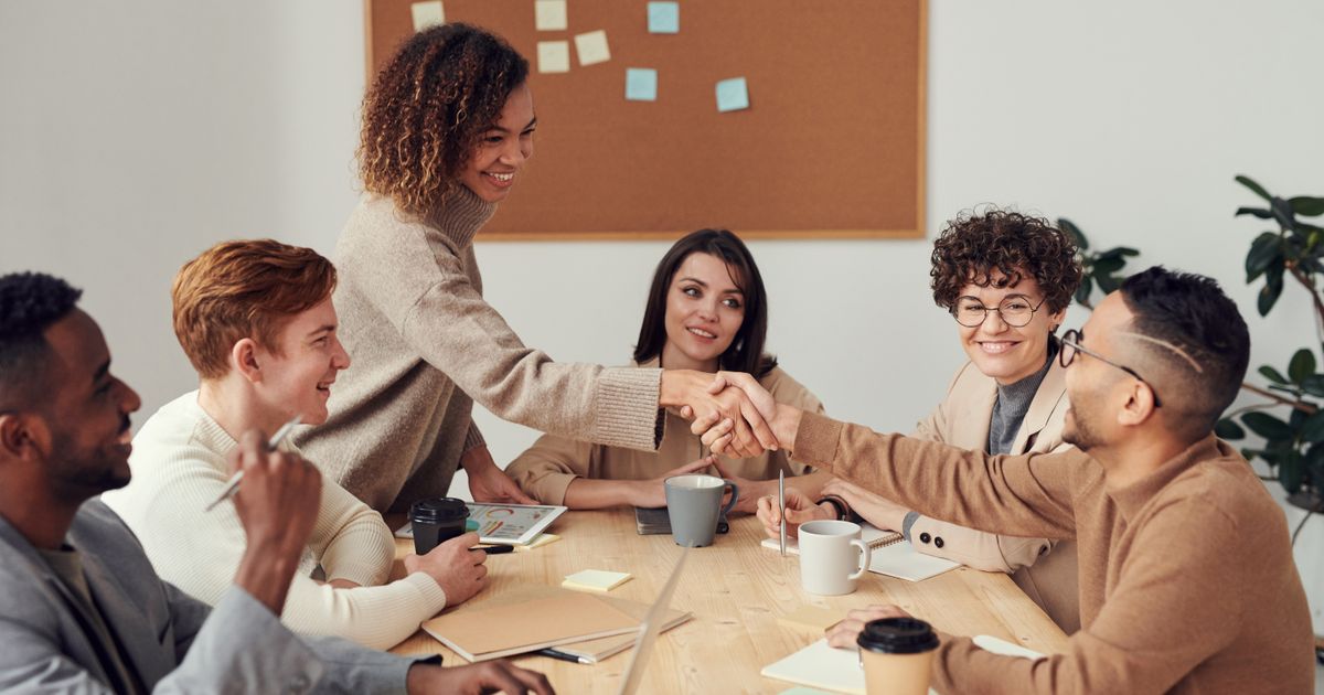 A sales team shaking hands around a conference table during a meeting.