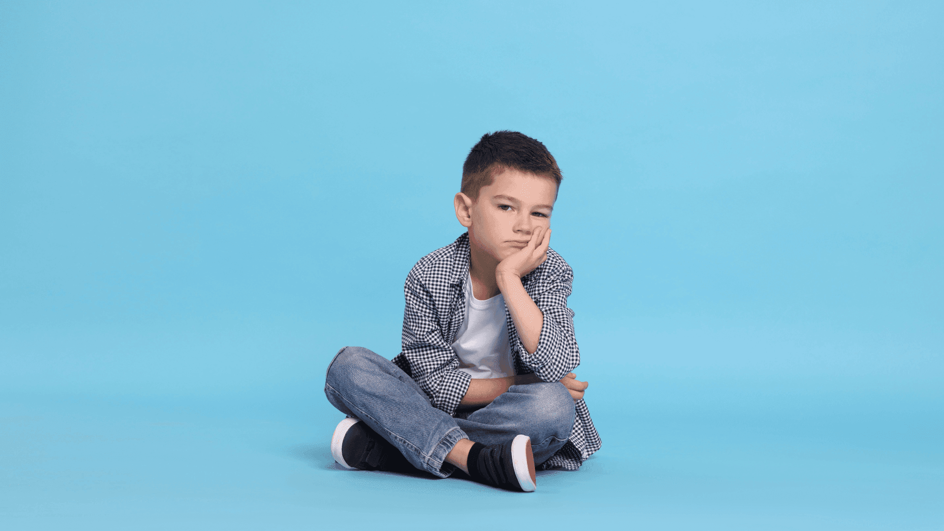 A boy sitting and looking fed up while trying to regulate his emotions.